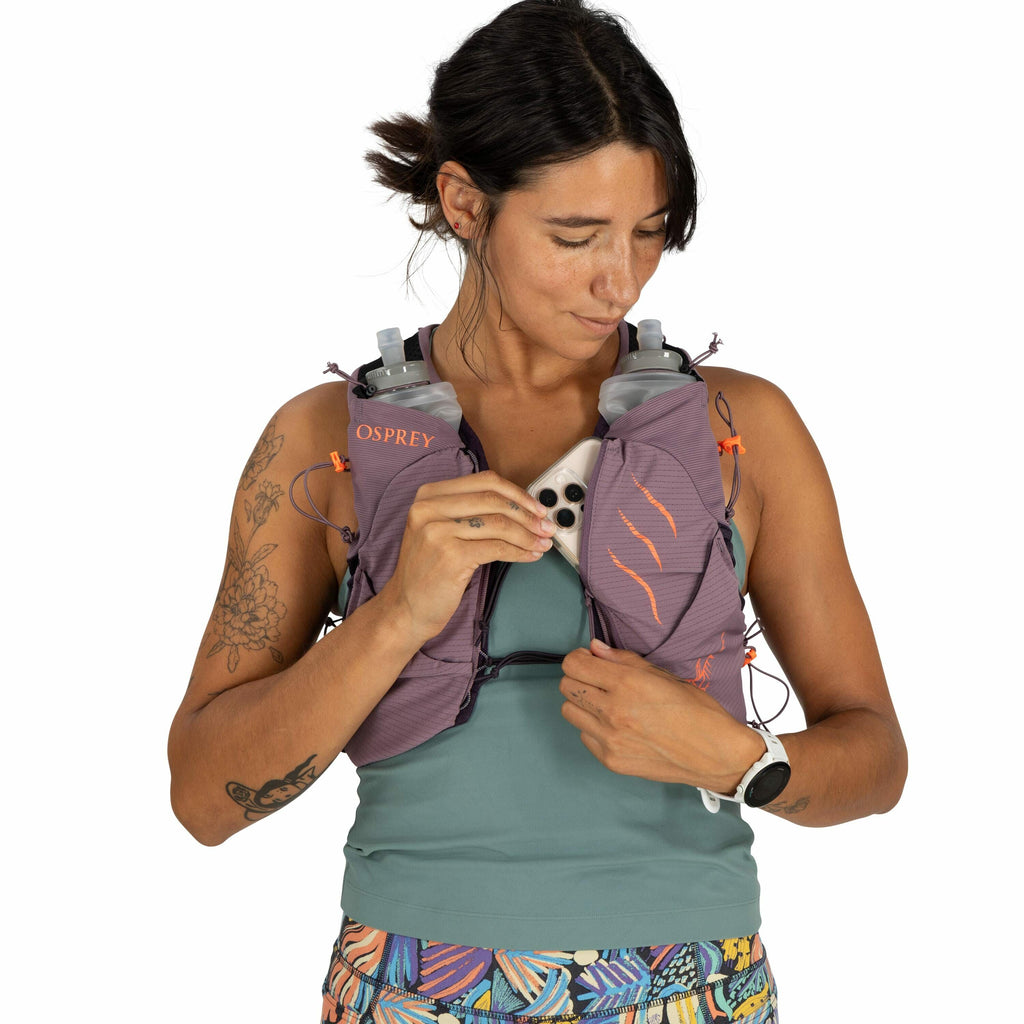 The image shows a person wearing a purple running vest with the "Osprey" logo on it. The vest is designed for carrying gear, as evidenced by the two soft water bottles in the front pockets. The person is holding a smartphone, which appears to be placed in