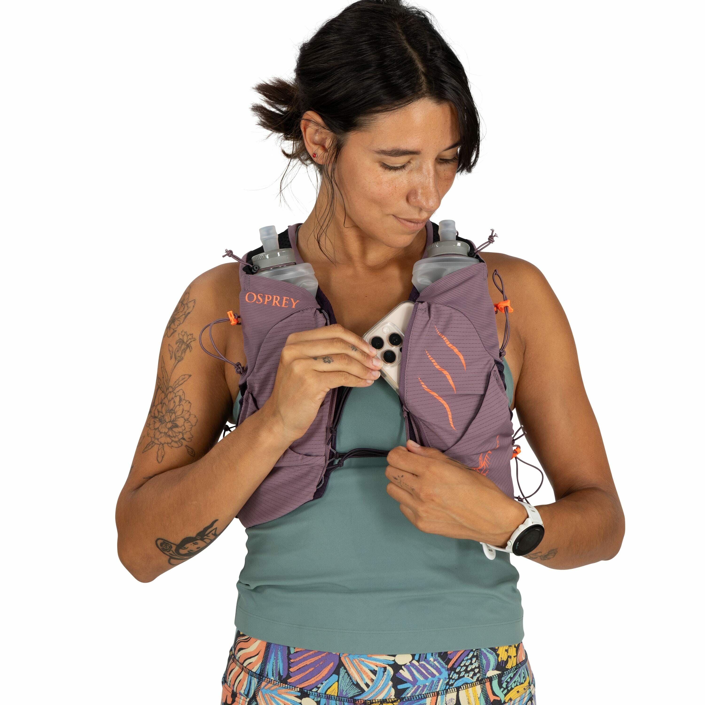 The image shows a person wearing a purple running vest with the "Osprey" logo on it. The vest is designed for carrying gear, as evidenced by the two soft water bottles in the front pockets. The person is holding a smartphone, which appears to be placed in