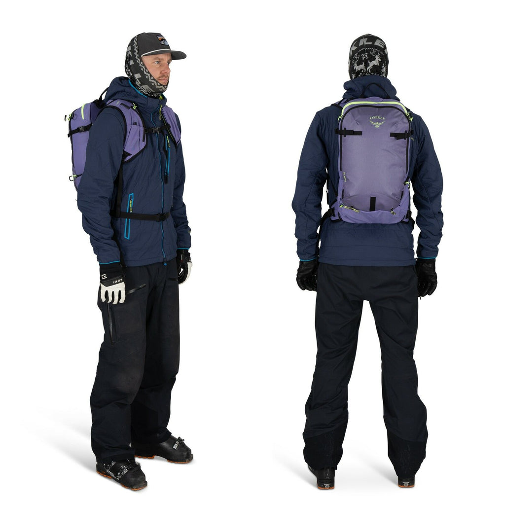 The image shows a person dressed in winter gear, both from the front and the back. The individual is wearing a dark blue jacket paired with black snow pants and black gloves. On their head, they have a hat and a scarf or balaclava, providing additional wa