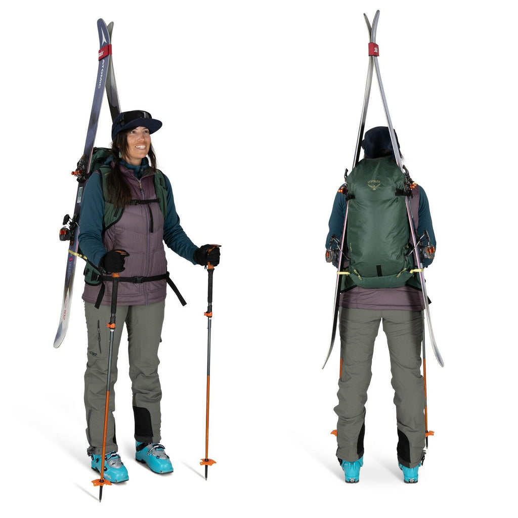 The image shows a person dressed in skiing gear, viewed from the front and back, standing in a studio setting. They are wearing a teal jacket layered under a purple vest, gray pants, and turquoise ski boots. The individual is equipped with a backpack that