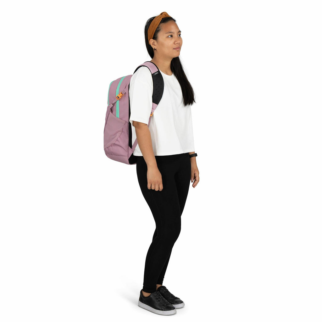 The image shows a woman standing and facing sideways. She is wearing a white, short-sleeved shirt and black leggings, paired with black sneakers. Her accessories include a mustard yellow headband and a black wristwatch. She is carrying a large, stylish ba