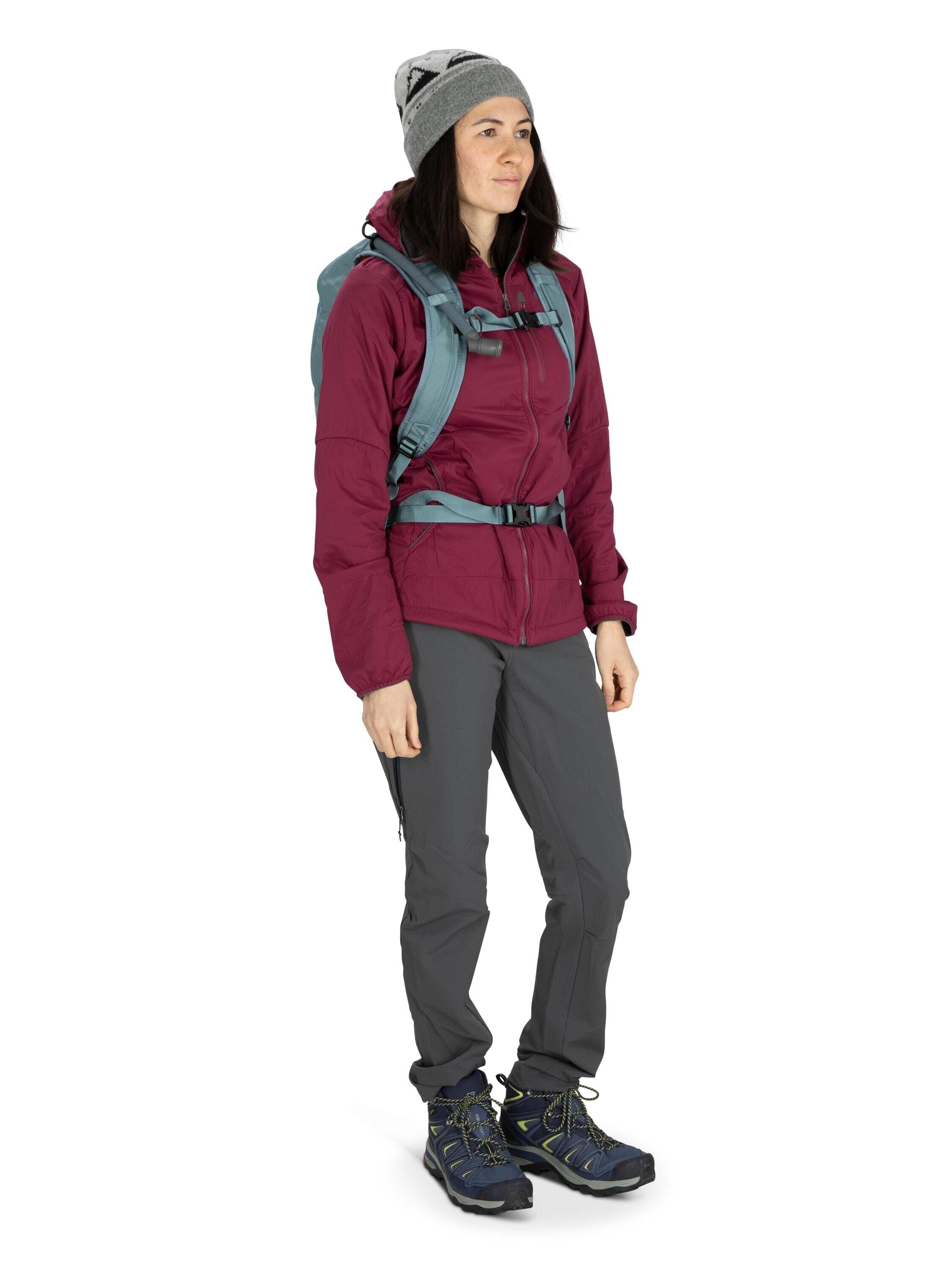 The image shows a person dressed for outdoor activities, such as hiking. They are wearing a dark maroon jacket, which appears to be insulated and weather-resistant, paired with gray pants that seem suitable for trekking or mountaineering. On their feet, t