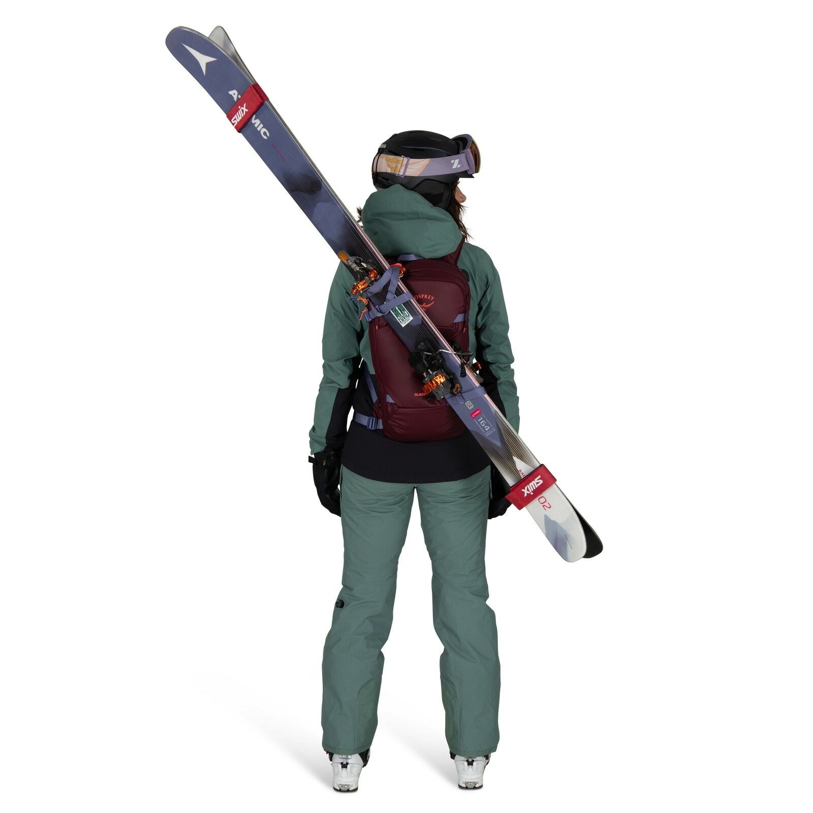 The image shows a person dressed in ski gear, viewed from the back. They are wearing a teal-colored ski jacket and pants, with a maroon backpack that securely holds a pair of skis diagonally across their back. The individual is also wearing black gloves a