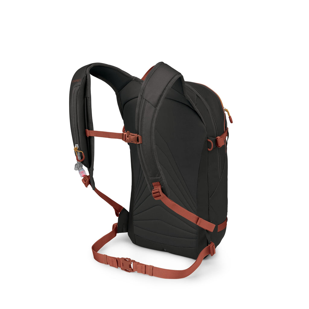 The image shows the back and side of a black backpack with contrasting rust-red straps and buckles. It features padded shoulder straps, a sternum strap with an emergency whistle, and a padded back panel with contoured stitching. There is also a waist belt