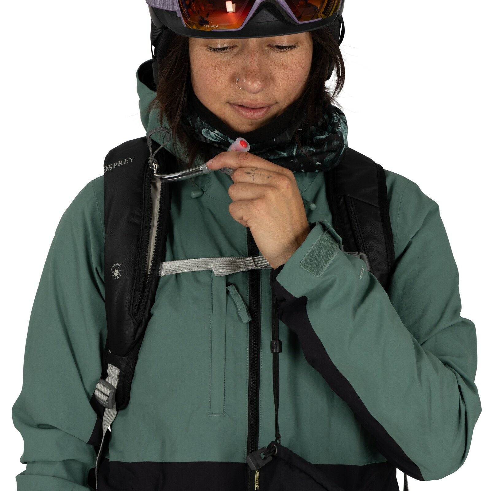 The image shows a person wearing a green and black outdoor jacket, suitable for cold weather or snow sports. They have a black Osprey backpack, which suggests they might be preparing for an outdoor activity such as hiking or skiing. The individual is hold