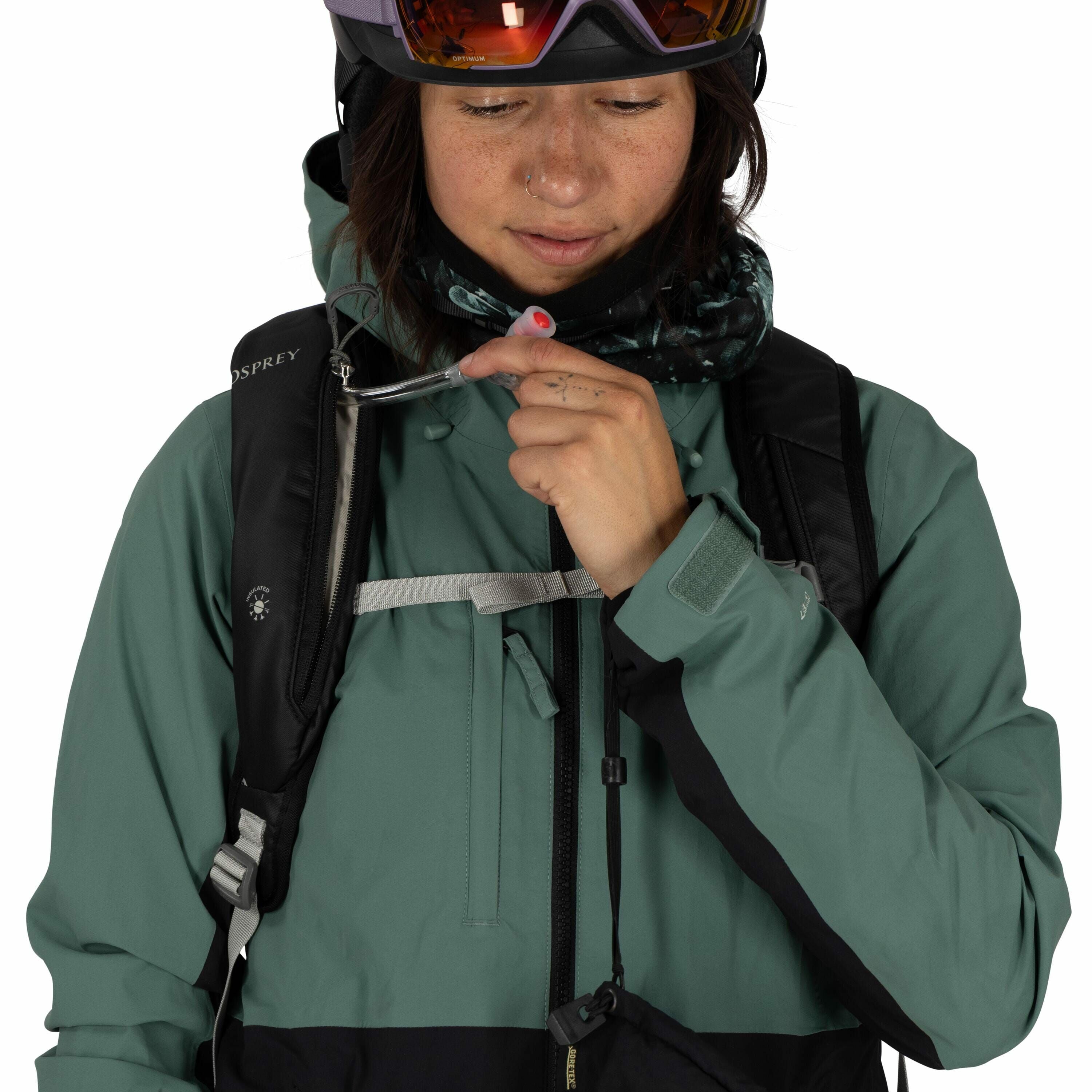 The image shows a person wearing a green and black outdoor jacket, suitable for cold weather or snow sports. They have a black Osprey backpack, which suggests they might be preparing for an outdoor activity such as hiking or skiing. The individual is hold