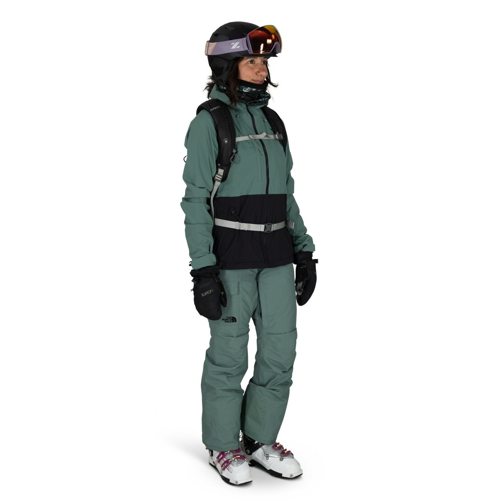 The image shows a person dressed in outdoor winter gear suitable for skiing or snowboarding. They are wearing a green and black The North Face jacket paired with matching green pants and black gloves. The outfit is accessorized with a backpack, and the pe