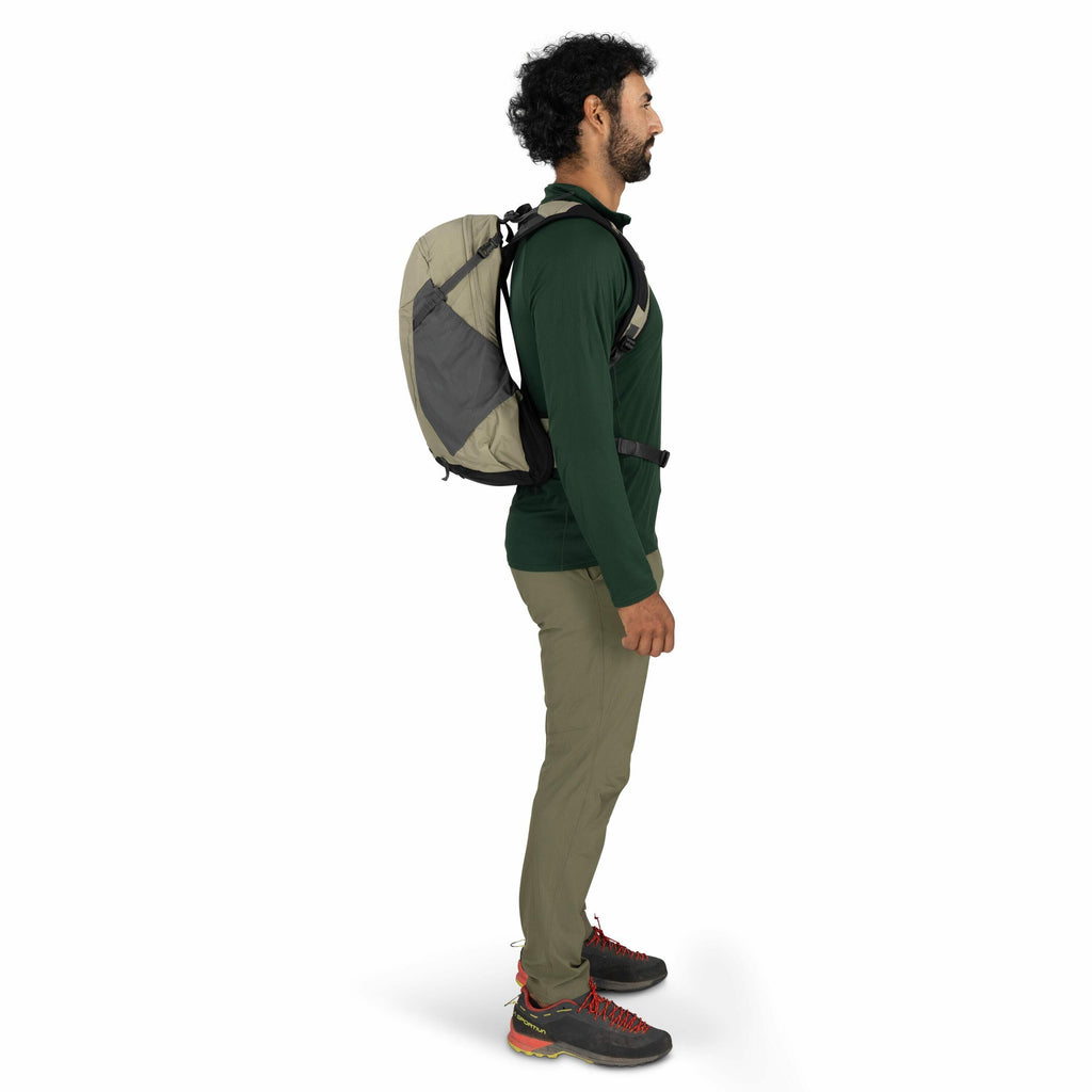 The images depict a person standing in profile, dressed in outdoor attire. They are wearing a green long-sleeved shirt, olive green pants, and black and red hiking shoes. The individual is carrying a beige and grey backpack with black straps. The posture