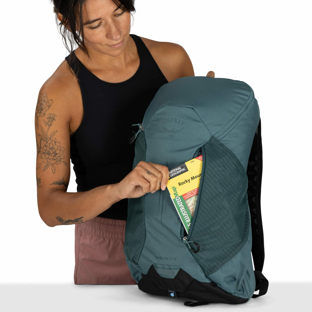 The image features a person holding a teal Osprey backpack, prominently showcasing the brand's logo. The person is placing a National Geographic Trails Illustrated map into one of the backpack's zippered side pockets. The map is for the Rocky Mountain reg