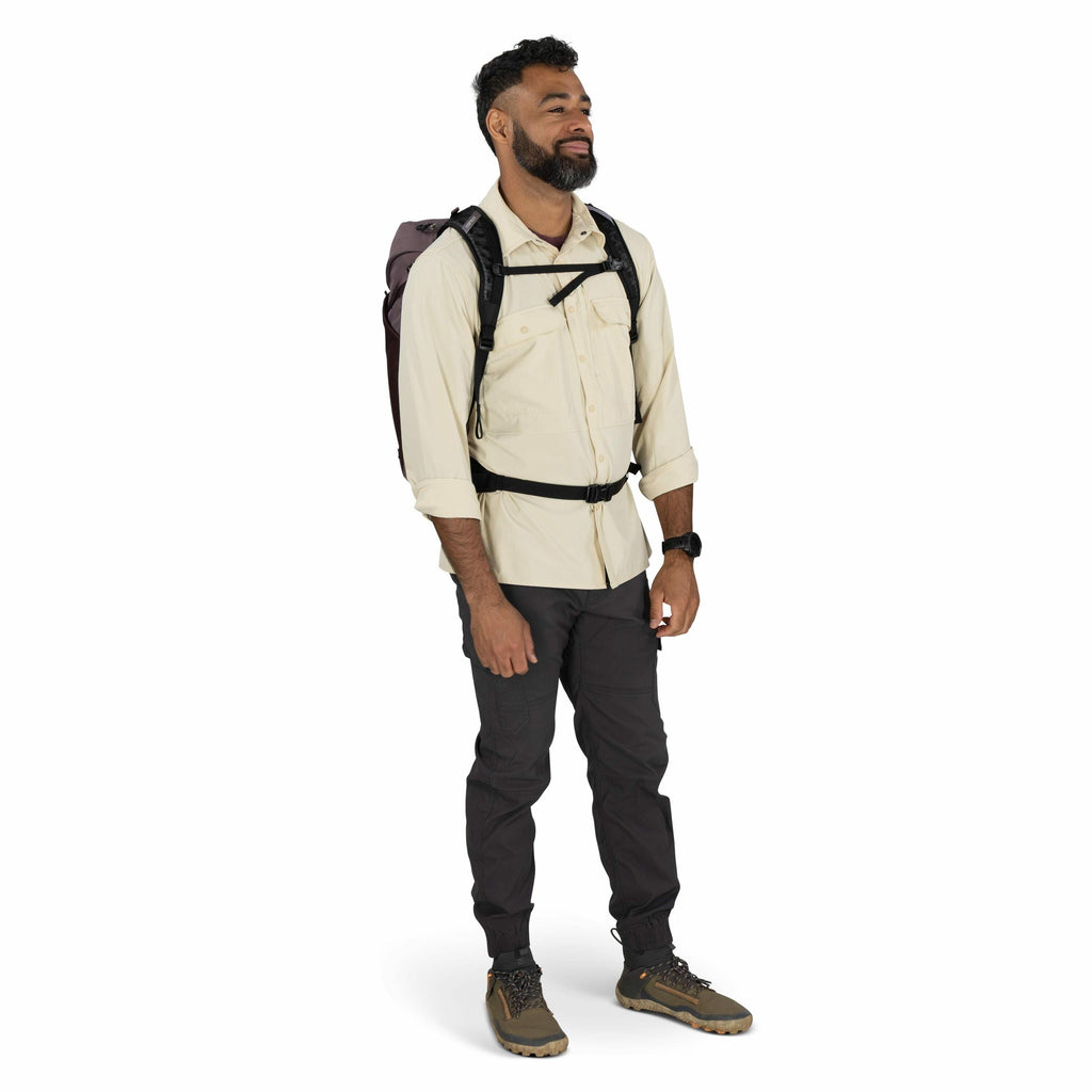 The image depicts a person standing against a plain white background. The individual is dressed in outdoor attire, including a beige long-sleeve button-up shirt, dark gray cargo pants, and brown hiking shoes with yellow laces. The person is wearing a dark