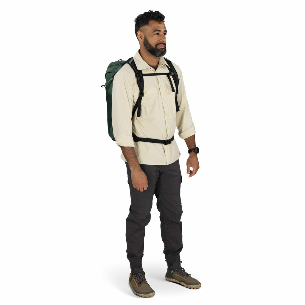 The image features a man dressed in outdoor gear, suggesting he is prepared for a hiking or camping excursion. He is wearing a light-colored, long-sleeved shirt with the sleeves rolled up, paired with dark cargo pants and outdoor shoes designed for rough