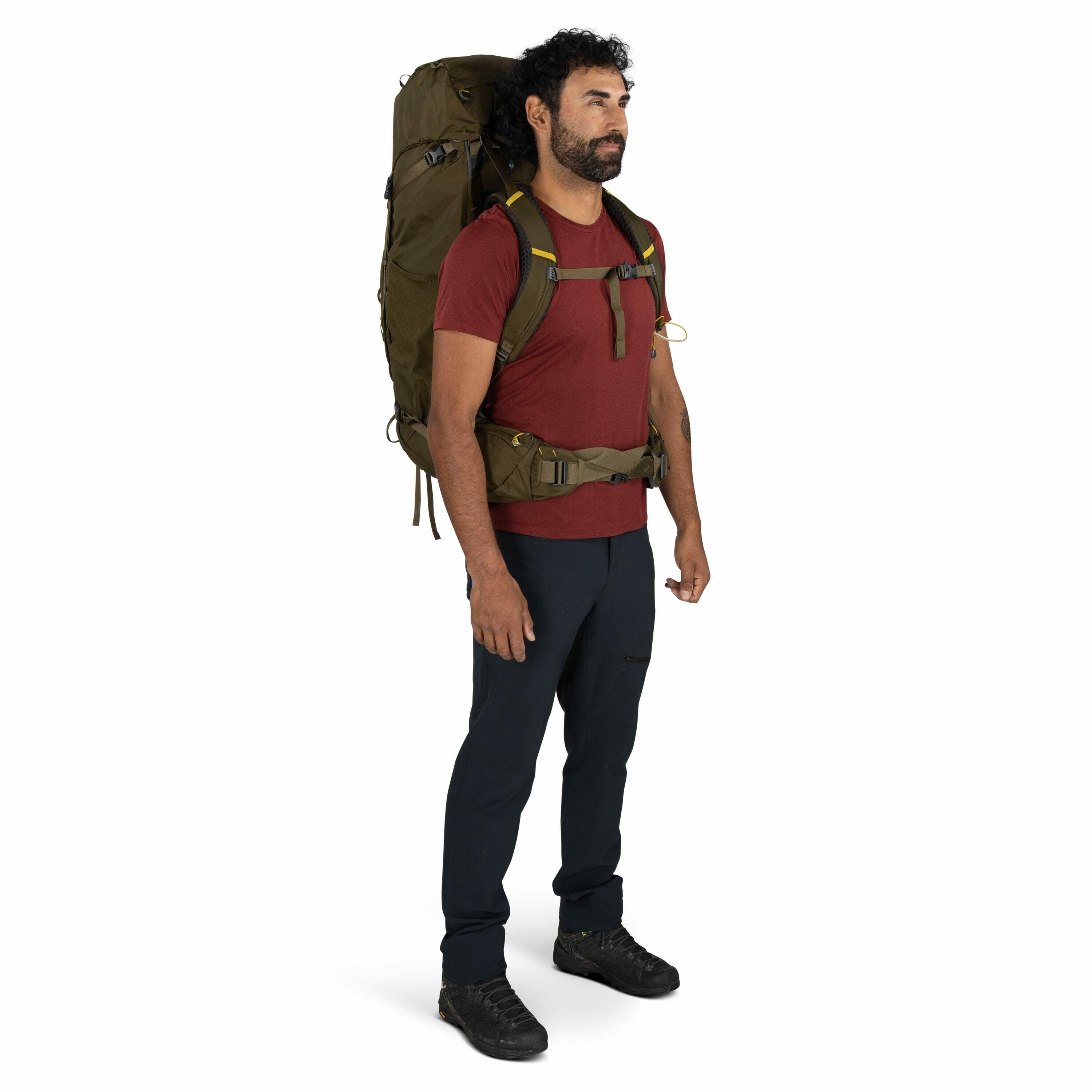The image shows a person standing upright wearing outdoor hiking gear, which includes a large olive green backpack that has multiple compartments and straps, providing a sturdy and adjustable fit. The person is dressed in a casual hiking outfit with a mar