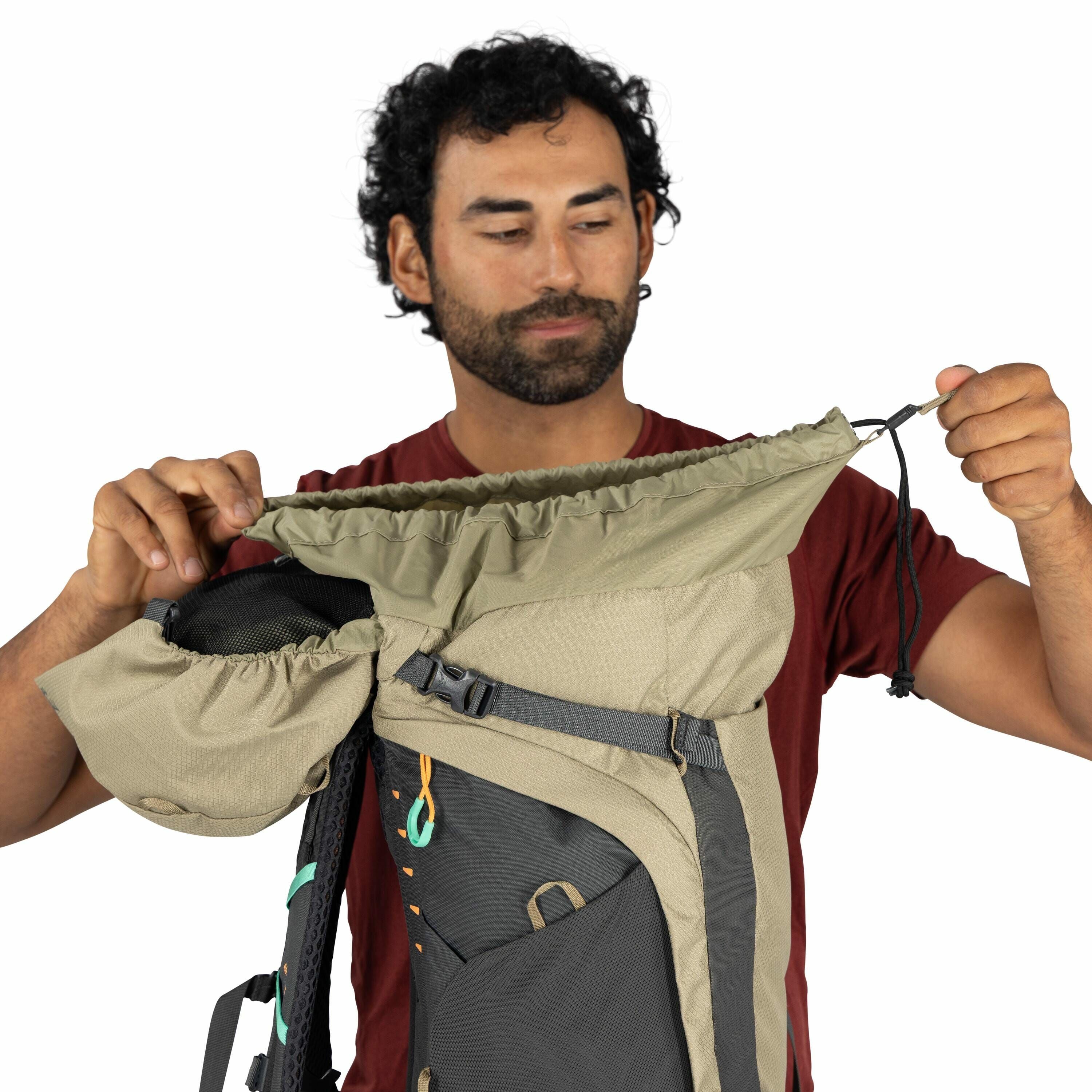 The image features a person holding a large outdoor backpack, showcasing its various compartments and design features. The backpack is primarily beige with some dark gray sections and is equipped with multiple straps and buckles for securing and adjusting