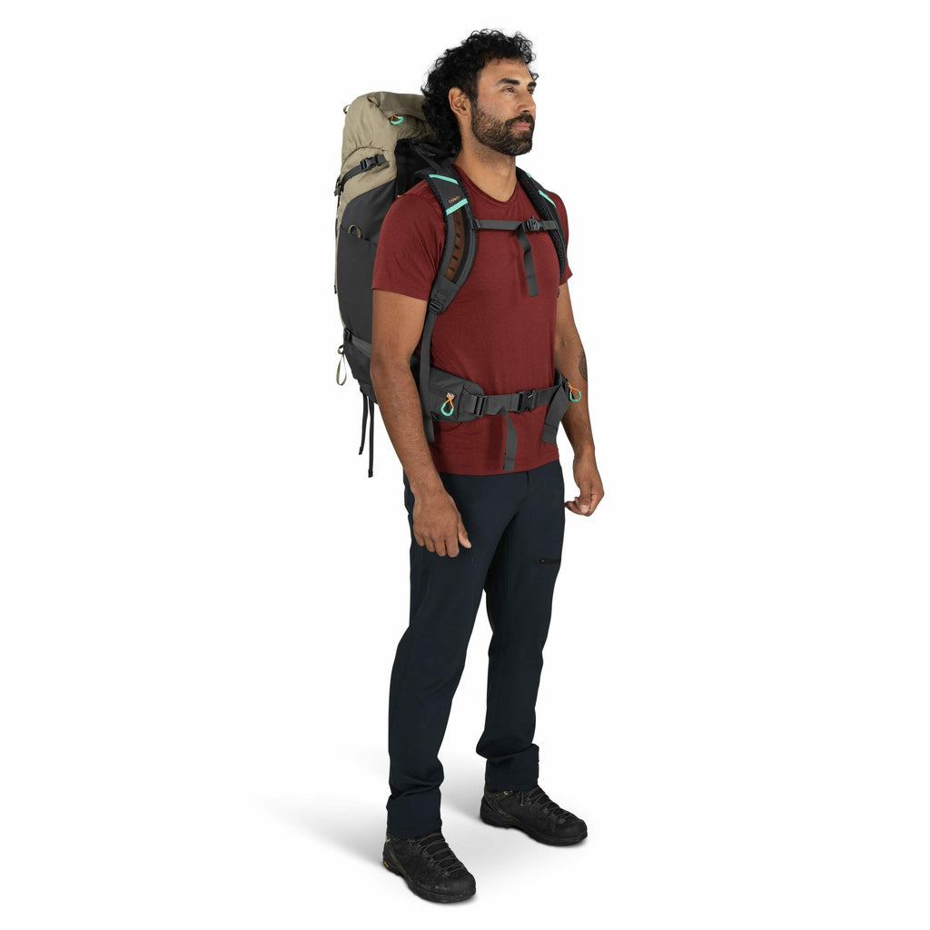 The image features a person standing upright wearing outdoor gear. The individual is dressed in a red short-sleeved shirt and dark pants, equipped with a large hiking backpack in tones of gray and beige, designed for outdoor adventures. The backpack is se