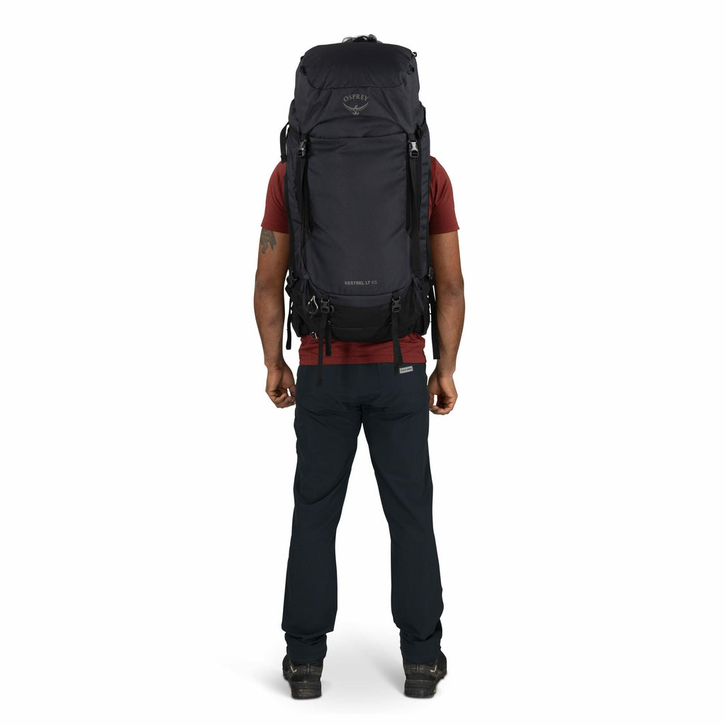 The image features a person standing with their back facing the camera, wearing a large backpack designed for hiking or outdoor adventures. The backpack is black and prominently displays the Osprey logo near the top, with "Kestrel 70" written below it, in