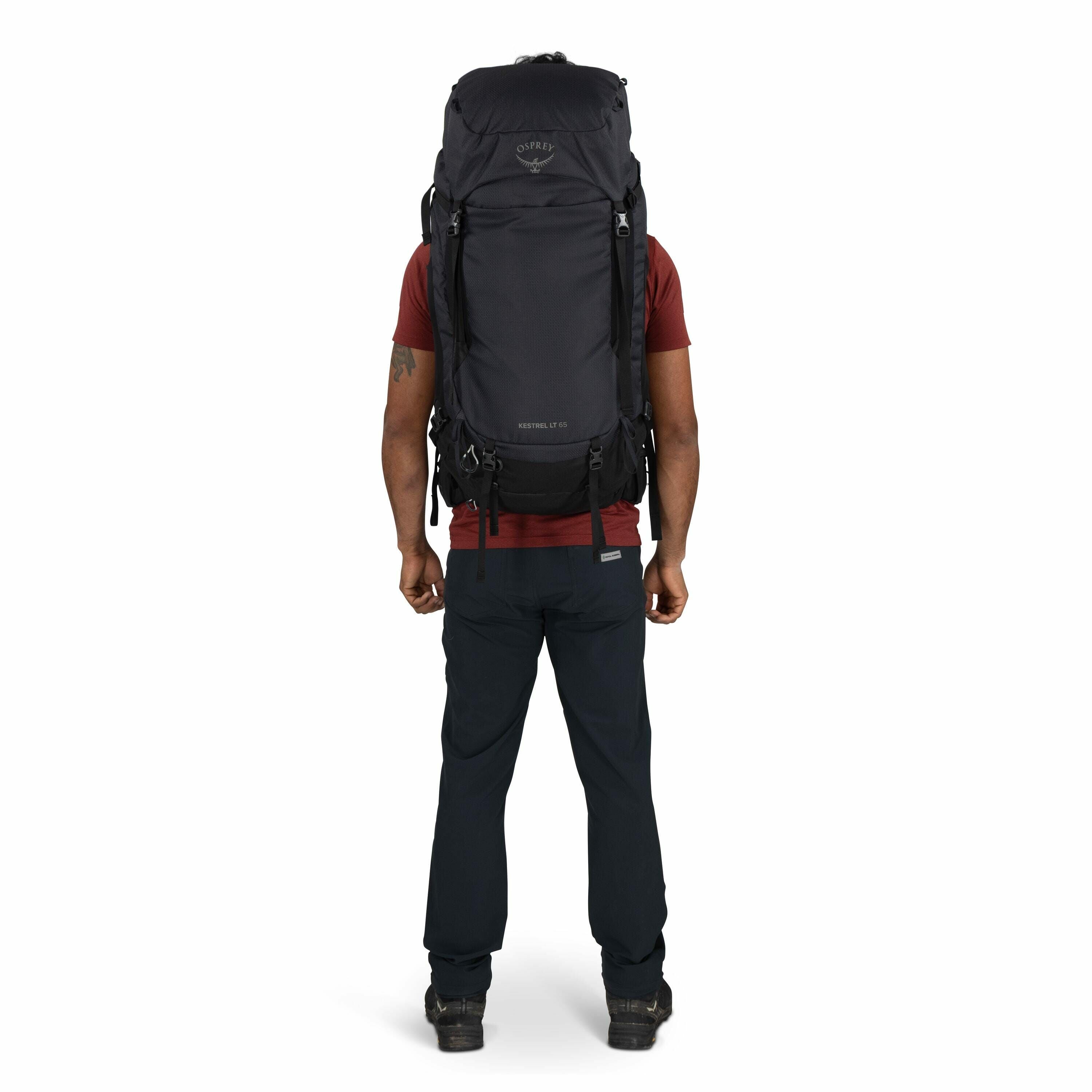 The image features a person standing with their back facing the camera, wearing a large backpack designed for hiking or outdoor adventures. The backpack is black and prominently displays the Osprey logo near the top, with "Kestrel 70" written below it, in