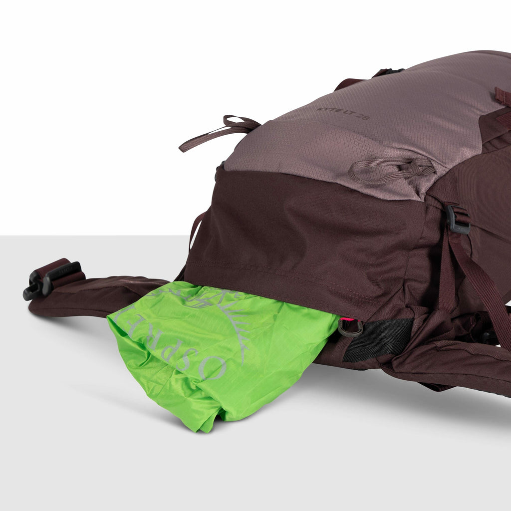 The image shows a close-up of a backpack, specifically the lower front section. The backpack is primarily brown and appears to be made of durable material, suggesting it's designed for outdoor use. A bright green item, labeled with the logo "Osprey" and a