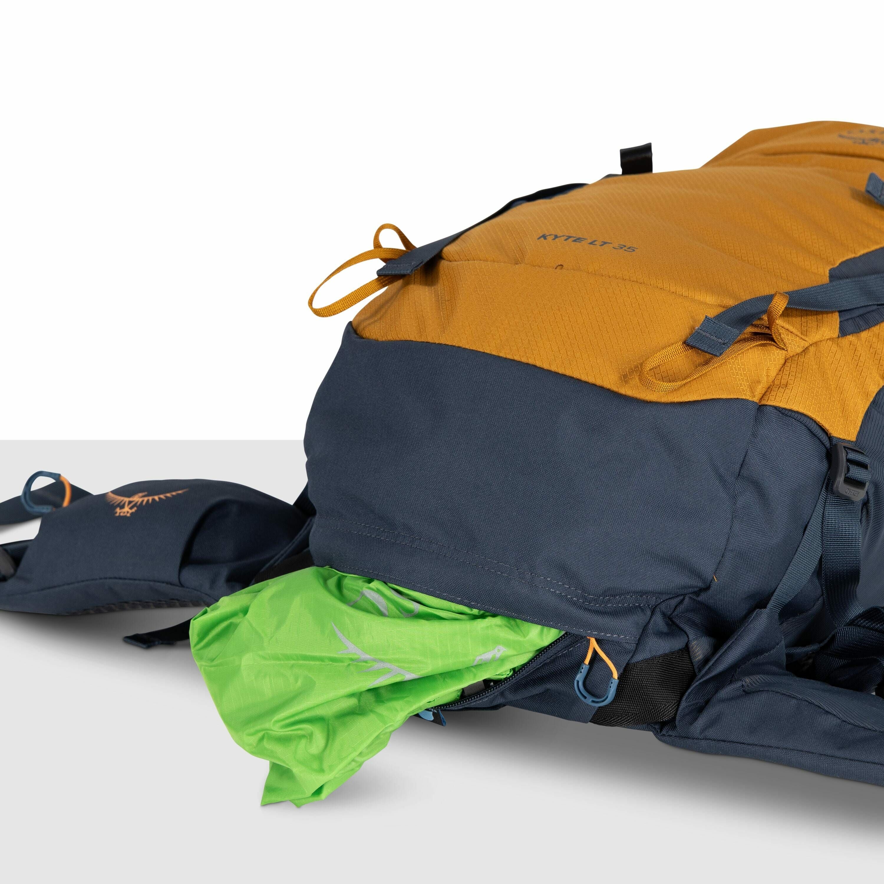The image features a close-up view of a backpack with a two-tone color scheme of mustard yellow and dark gray. The backpack is identified as a KESTREL 38 model, which is subtly printed on the yellow fabric. Part of the dark gray section is unzipped, revea