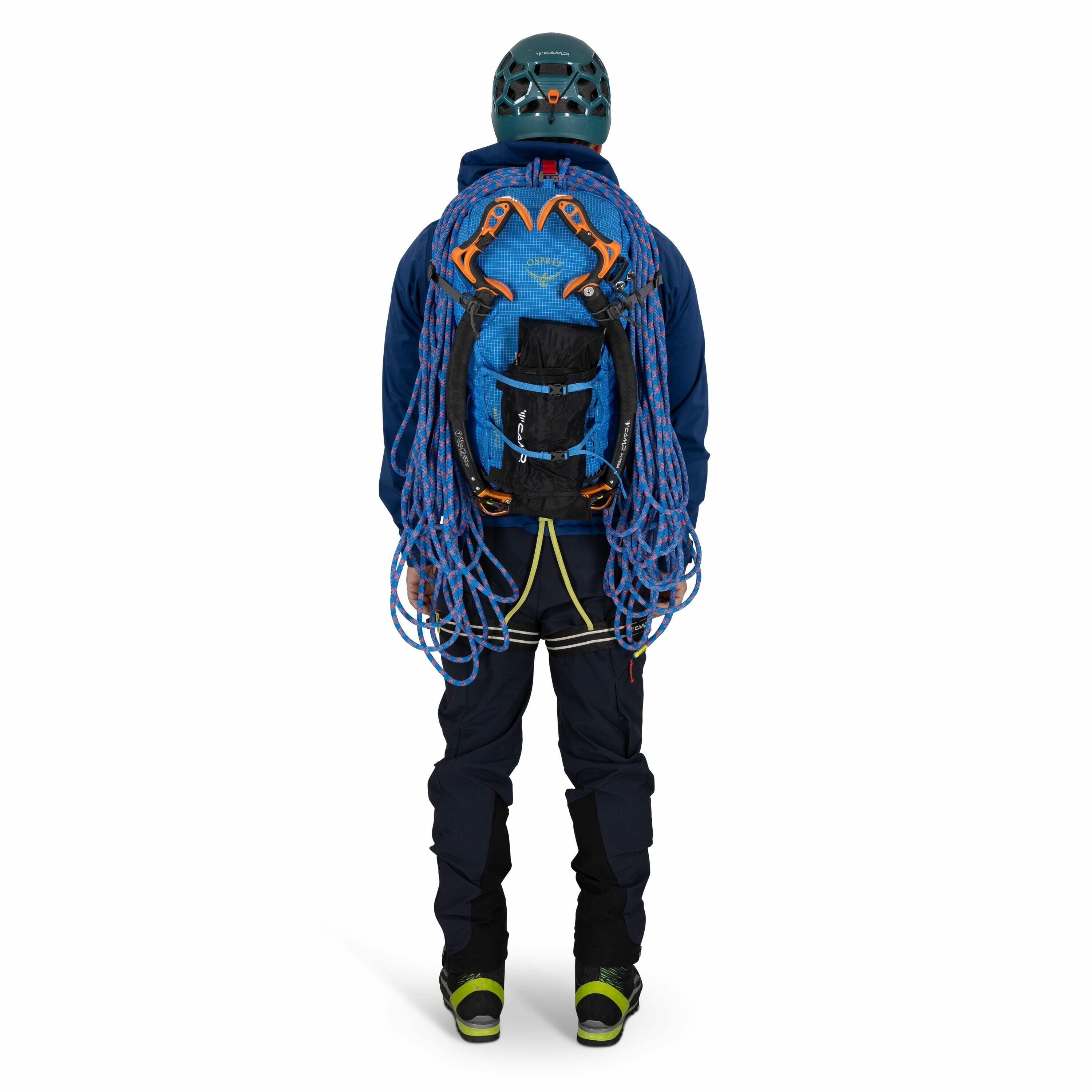 The image shows a person dressed in full climbing gear, standing with their back facing the camera. They are wearing a teal helmet and a blue backpack, which has climbing ropes neatly coiled and secured onto it. The person is dressed in a navy blue climbi