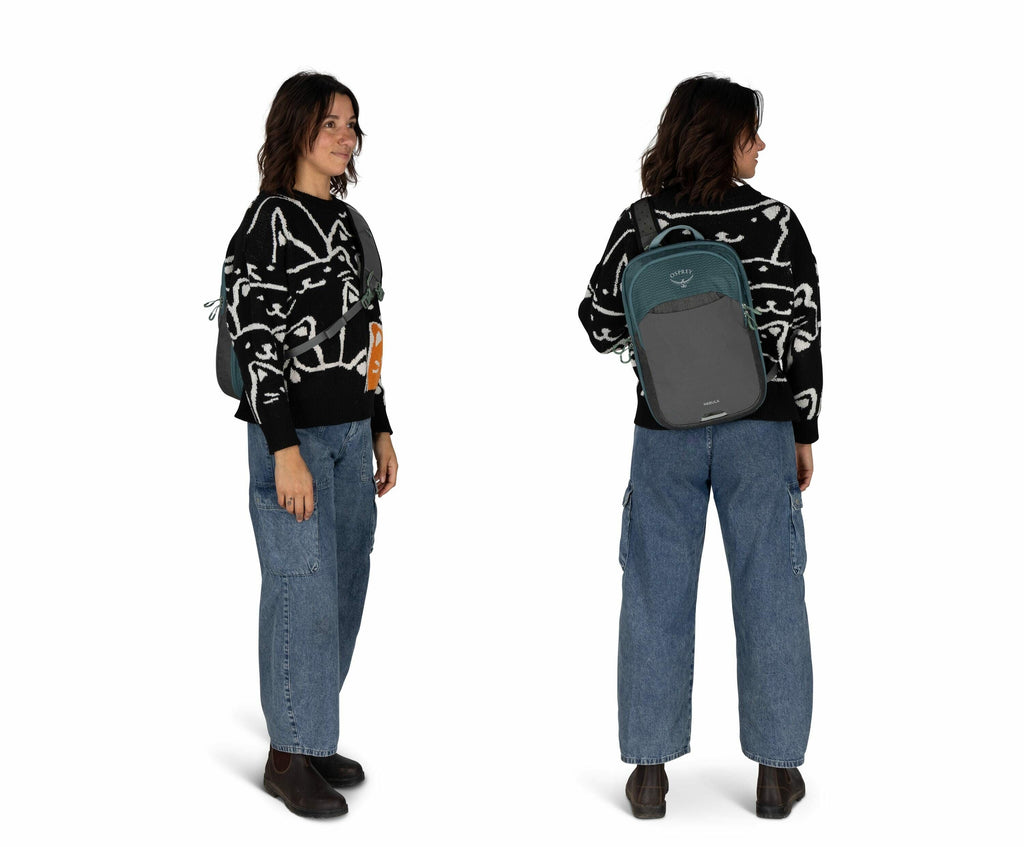 The image shows a person standing in a relaxed pose. They are wearing a black sweater with abstract white line art, paired with loose-fitting blue jeans. On their feet are dark ankle boots, and they are carrying a small, green backpack with black straps o