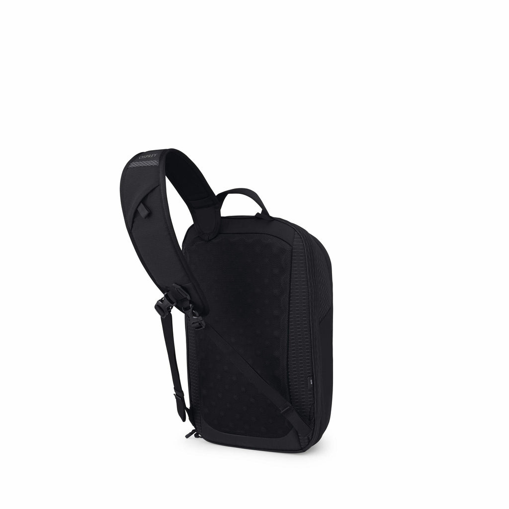The image depicts a black sling backpack with a modern and sleek design. It features a single, adjustable shoulder strap that is padded for comfort. The backpack appears to have a streamlined, rectangular shape with rounded corners, and it has a subtle do