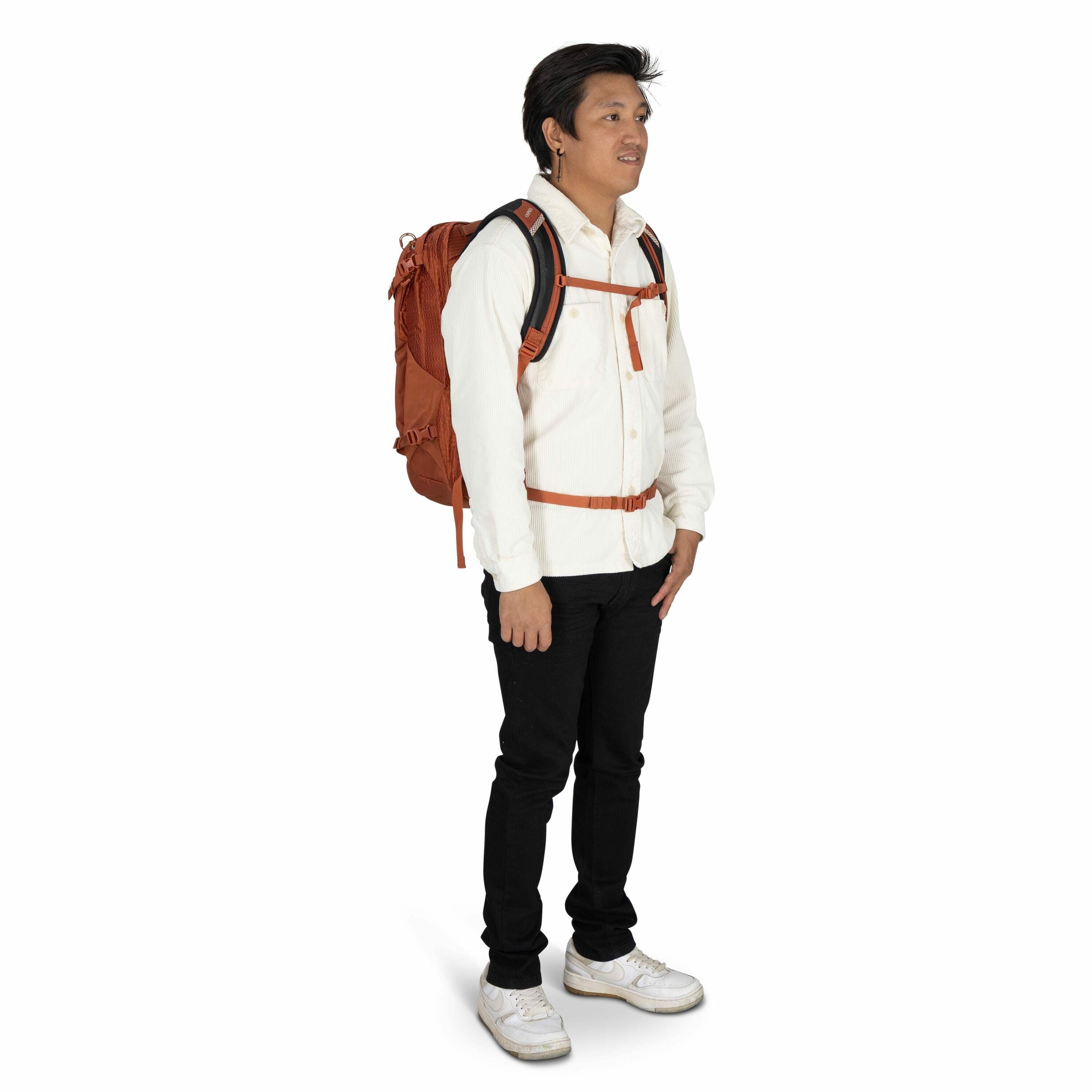 The image shows a person standing against a white background, wearing a casual yet coordinated outfit. The individual is dressed in a white button-up shirt and black pants, paired with white sneakers. They have a rust-colored backpack, which is secured wi
