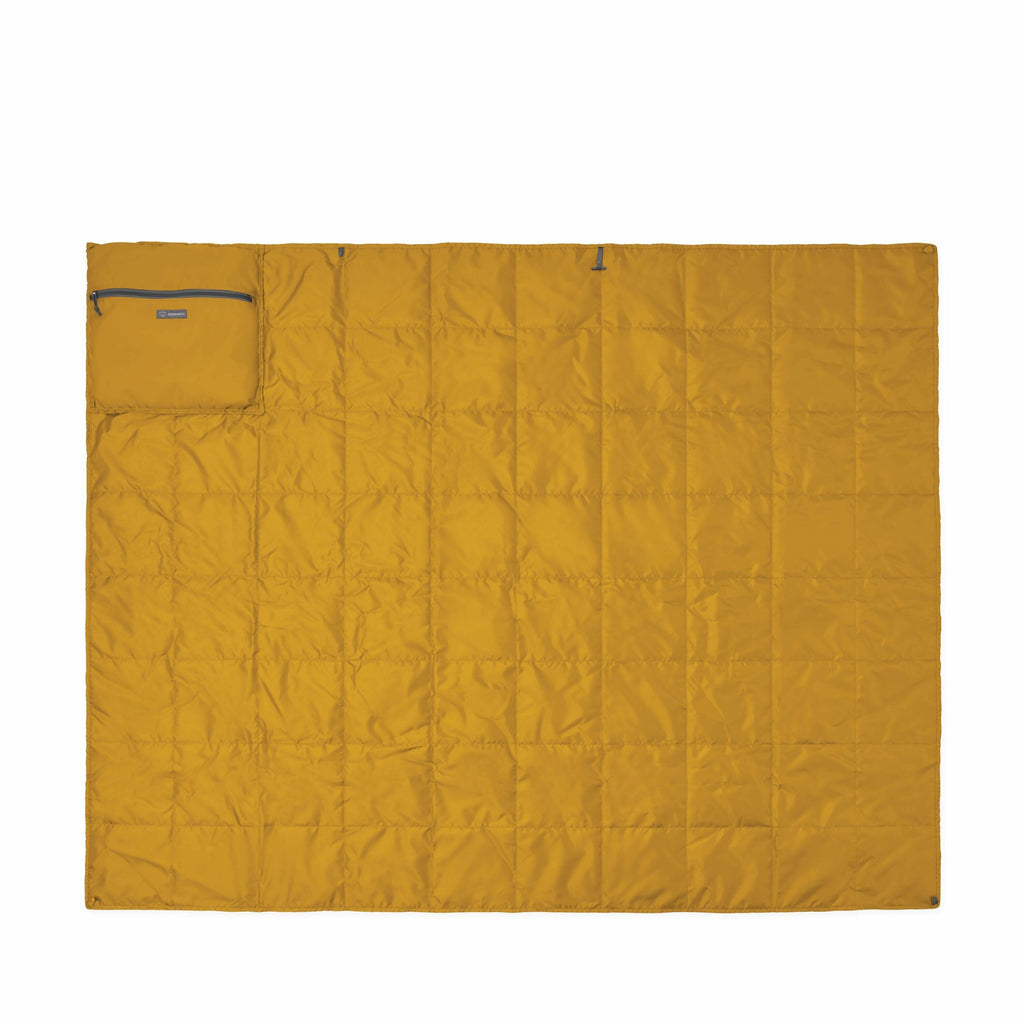 The image shows a rectangular quilt laid flat against a white background. The quilt is a mustard yellow color and appears to be padded or insulated, as indicated by the stitching pattern that creates small square sections. On the upper left corner, there