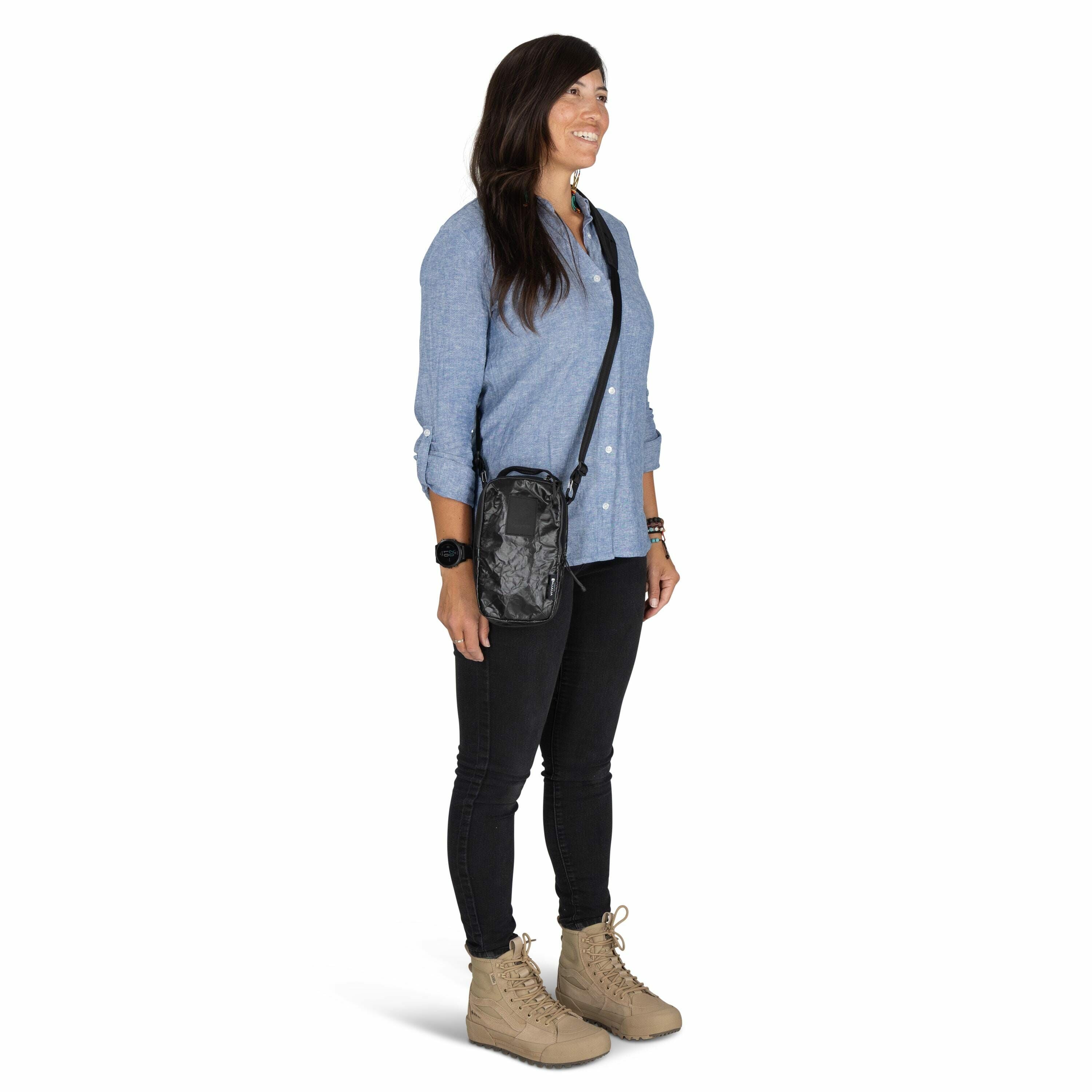 The image shows a woman standing in a relaxed pose, wearing a casual yet stylish outfit. She is dressed in a light blue button-up shirt paired with dark fitted jeans, which complement her ensemble. Her accessories include a black wristwatch and a black cr