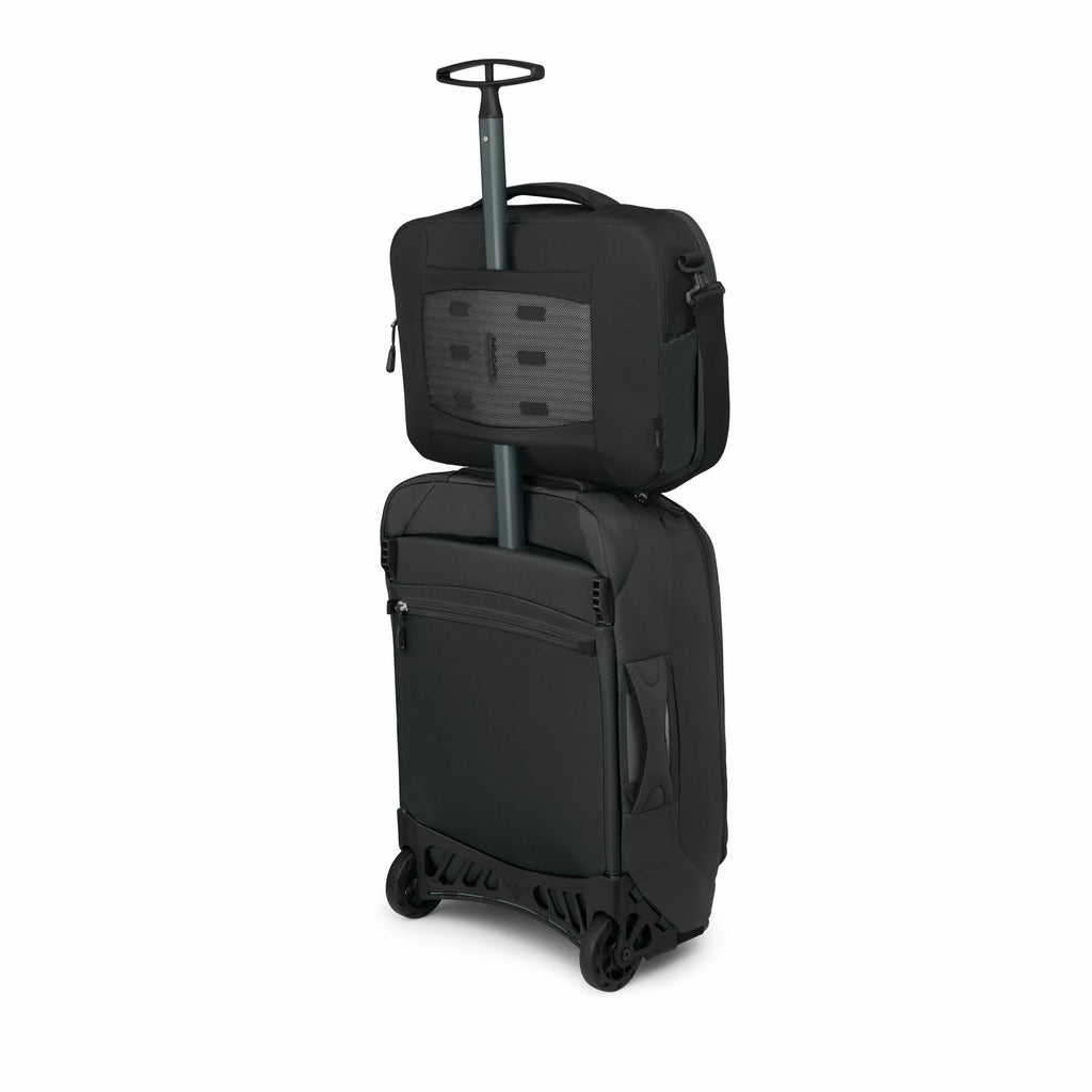 The image depicts a black, hard-shell carry-on suitcase with a retractable handle. Sitting on top of the suitcase, secured by the handle, is a smaller black travel bag with multiple compartments, likely designed for easy access to essential items. The sui