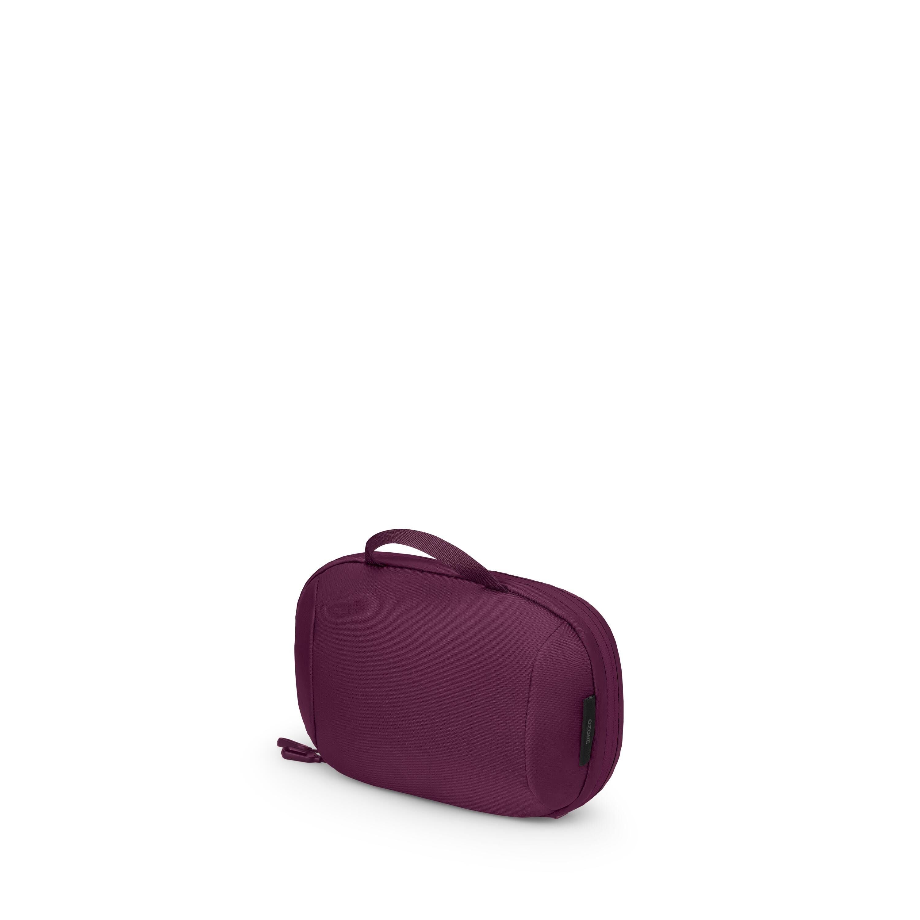 The image shows a compact, oval-shaped travel pouch in a rich purple color. It has a small top handle and a zipper that runs around the side, with a zipper pull visible at the lower left corner. A small black tag is attached on the right side seam. The po