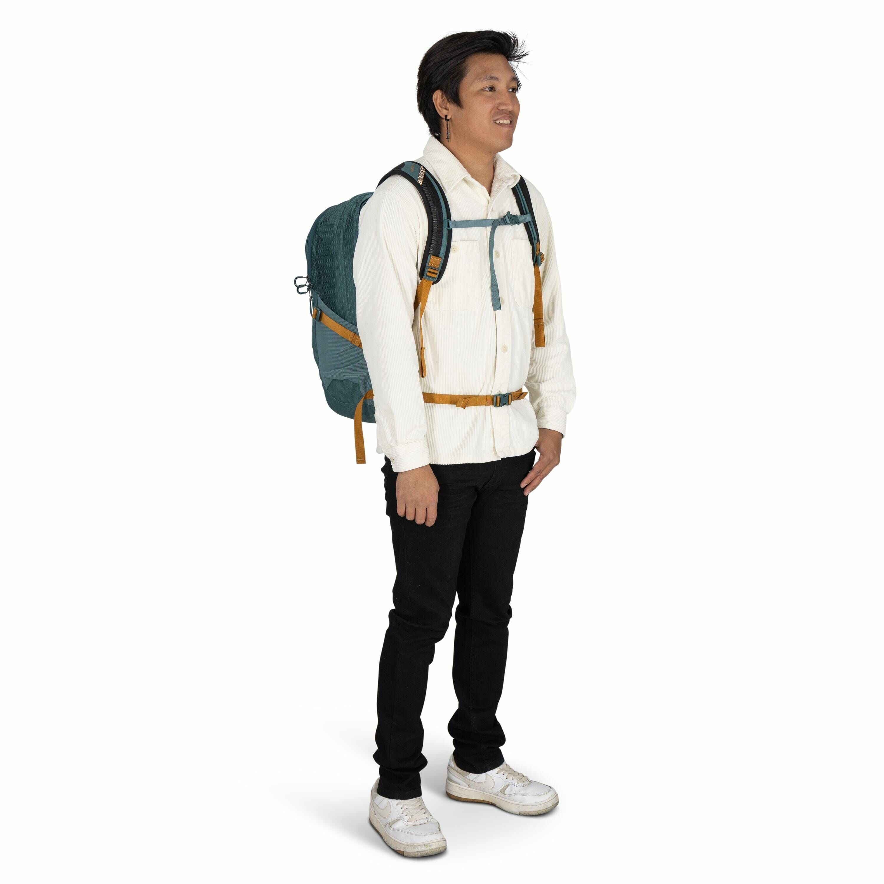 The image depicts a man standing wearing casual attire suitable for an outdoor or travel setting. He is wearing a white shirt with buttoned pockets and black pants, paired with white sneakers that have slight wear marks, suggesting frequent use. He is car