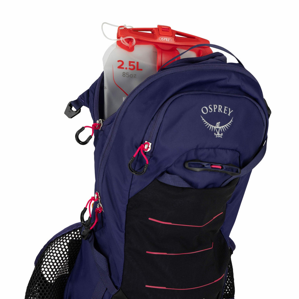The image shows a close-up view of a blue Osprey backpack with a focus on its hydration system. Inside the partially open top compartment, a transparent hydration reservoir is visible, which is marked with a red measurement indicating a 2.5-liter (85 oz)
