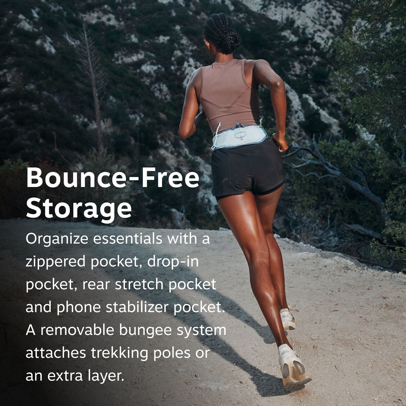 The image shows a woman running on a dirt trail surrounded by greenery and mountainous terrain. She is wearing a sleeveless brown top and black shorts, and there is a light blue waist pack with a visible logo on it labeled "Osprey." The waist pack is high