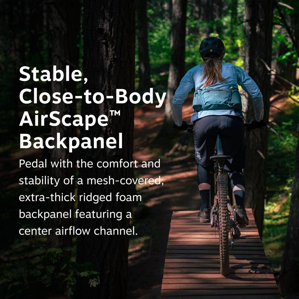 The image features a person biking on a narrow wooden path through a dense forest. The biker is wearing a light blue jacket and a matching backpack, along with a helmet and biking gloves. Sunlight filters through the trees, creating a mix of light and sha