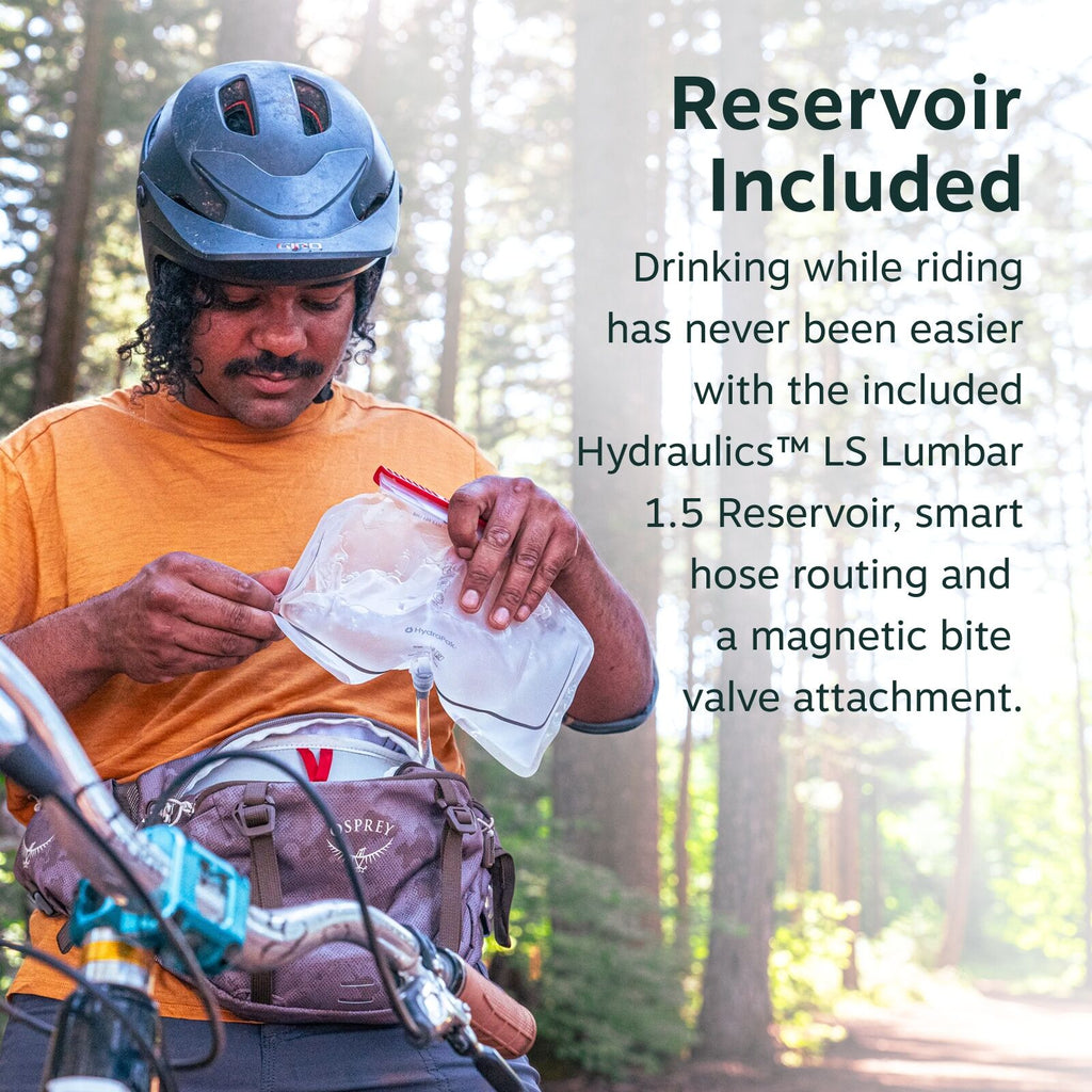 The image shows a person wearing a helmet and a casual orange t-shirt, engaged in an outdoor setting with tall trees in the background. They are holding a clear Hydraulics? LS Lumbar 1.5 reservoir in their hand, which is connected to a hose for easy acces