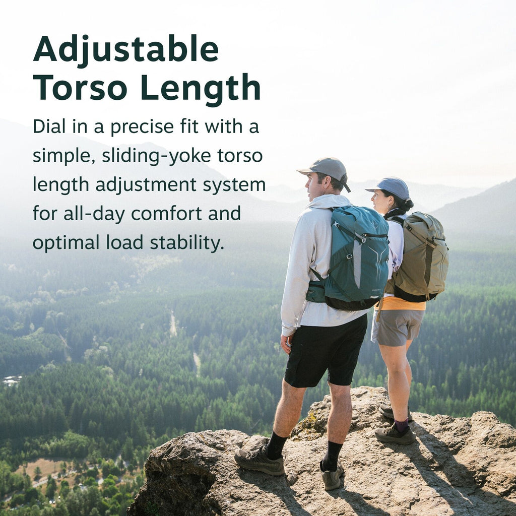 The image features two hikers standing on a rocky cliff overlooking a scenic landscape filled with lush green forests and distant mountain ranges. Both individuals are wearing outdoor attire, including hats and backpacks, as they take in the expansive vie