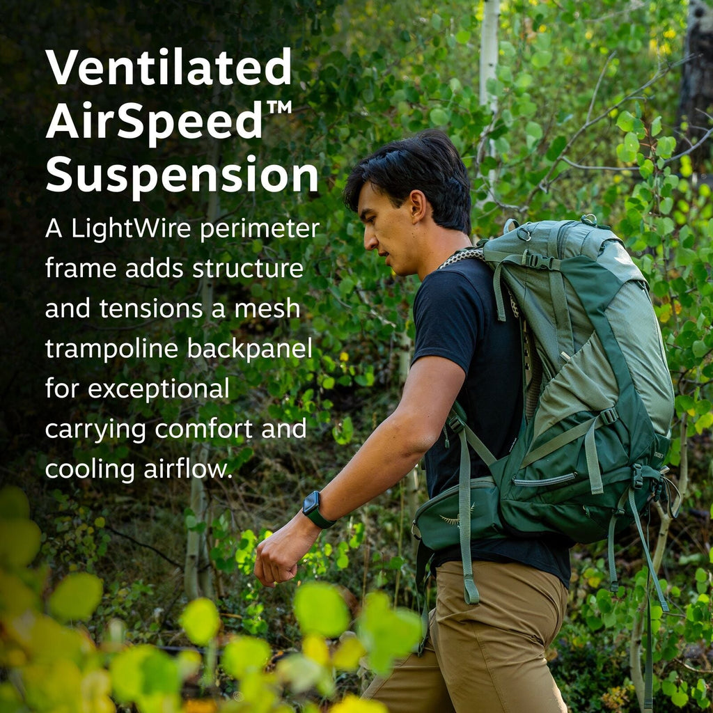 The image features a person hiking in a lush forest environment, surrounded by vibrant green leaves and natural scenery. They are wearing a black shirt and tan pants, carrying a large green backpack that is designed for outdoor activities. The backpack is
