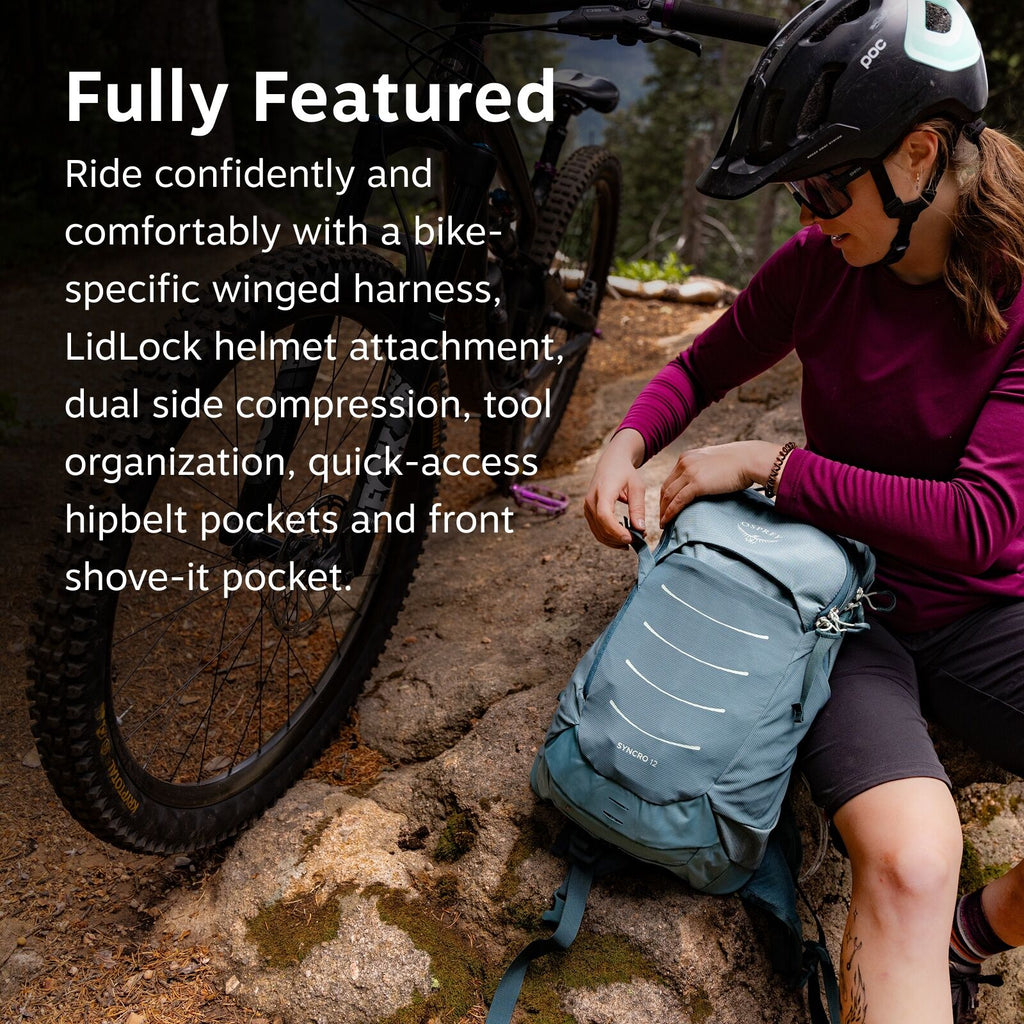 In the image, a person wearing a helmet is sitting on a rocky surface with a bicycle visible behind them. They are dressed in a long-sleeved maroon shirt and dark shorts and are adjusting or examining a blue backpack, which prominently features the Osprey