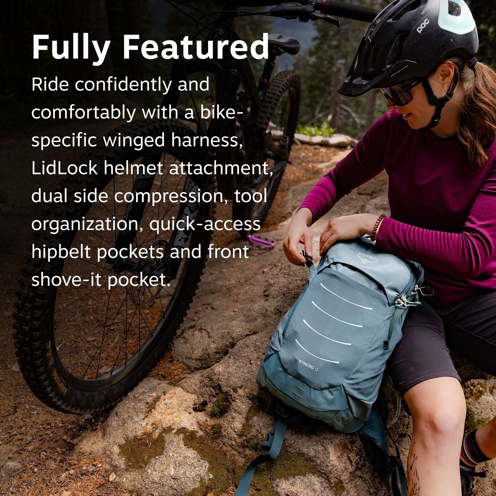In the image, a person wearing a helmet is sitting on a rocky surface with a bicycle visible behind them. They are dressed in a long-sleeved maroon shirt and dark shorts and are adjusting or examining a blue backpack, which prominently features the Osprey