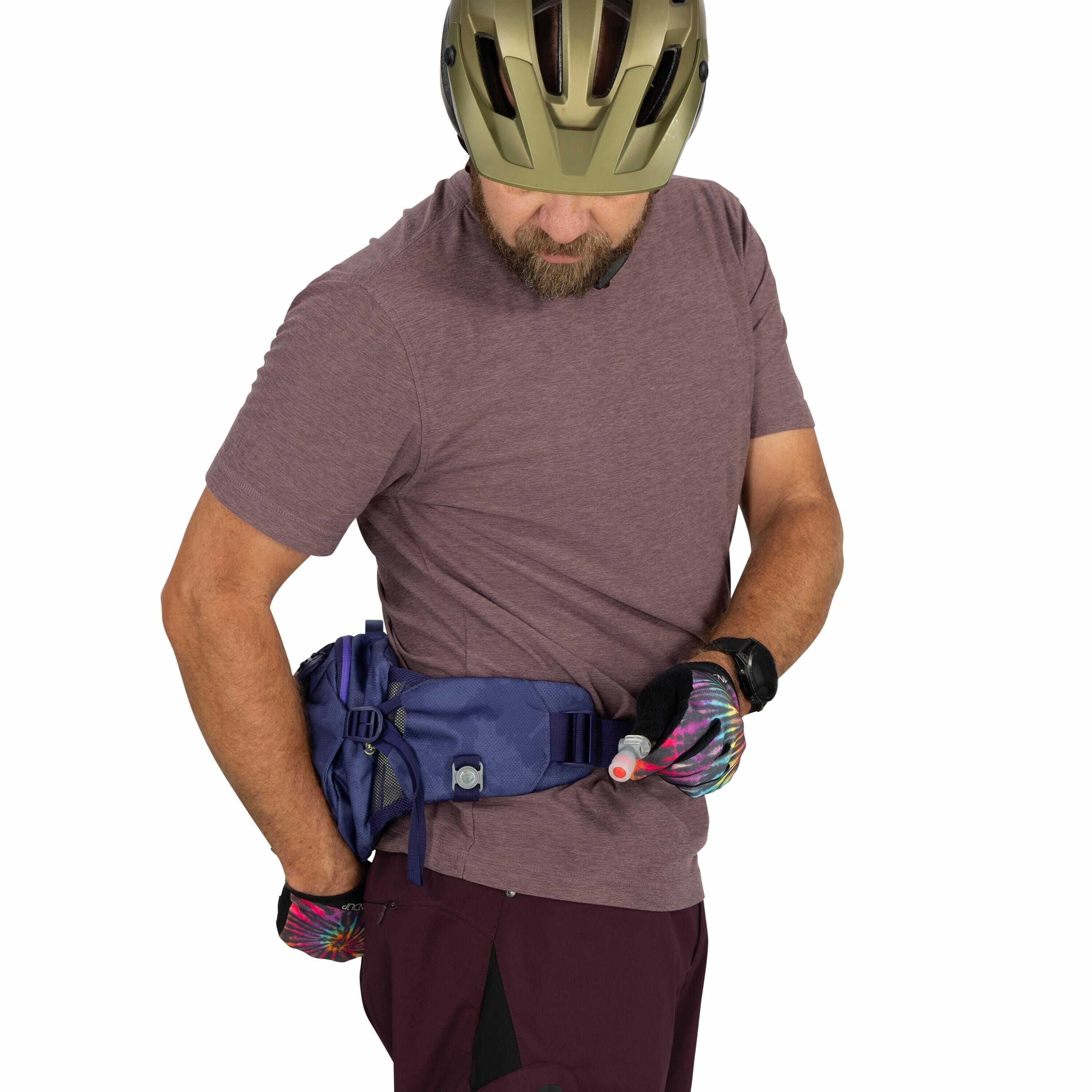The image shows a person wearing a cycling helmet and a casual outfit that includes a maroon shirt and matching maroon pants with black details. The person is wearing colorful cycling gloves and a black smartwatch on their wrist. They have a blue waist pa
