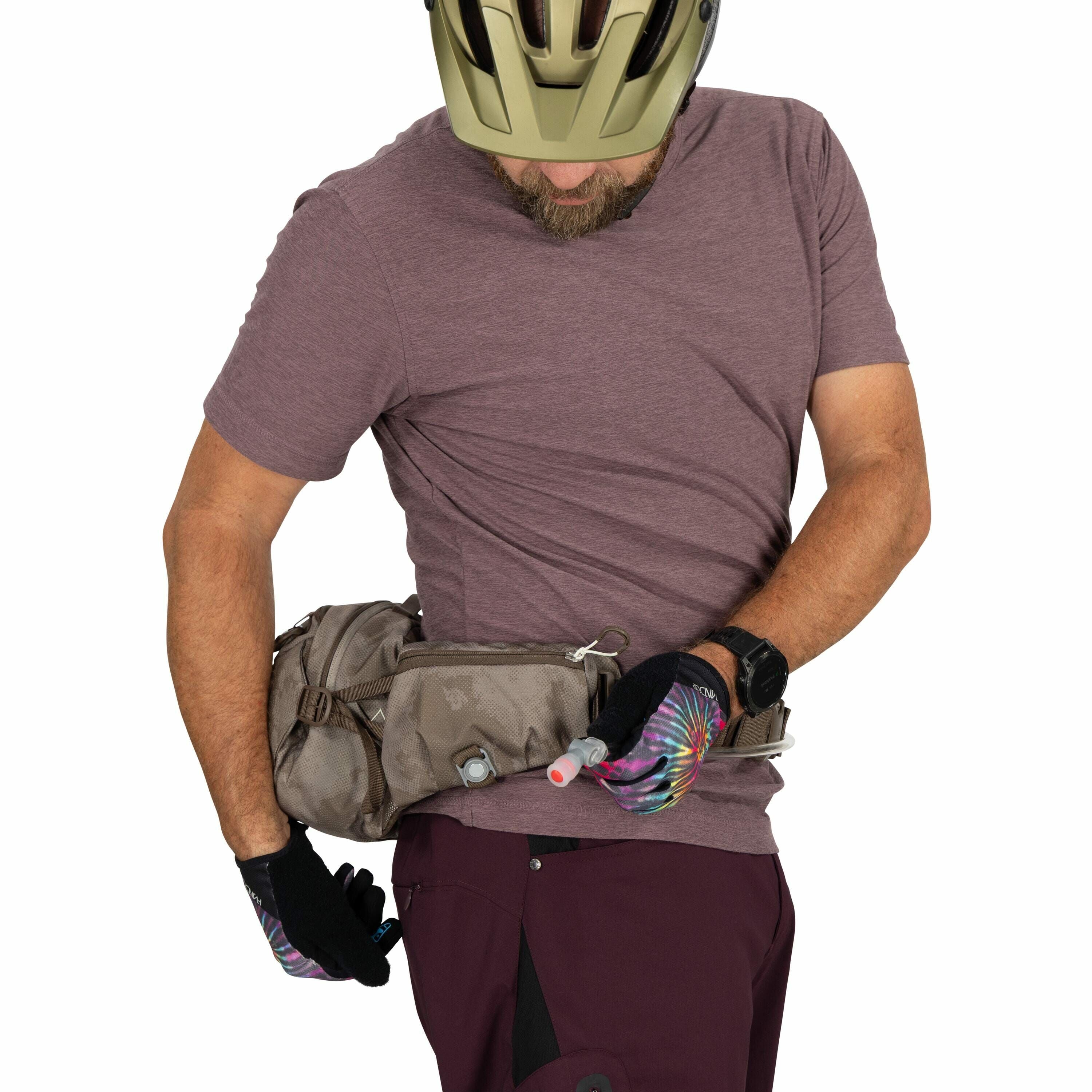 The image shows a man wearing a bike helmet and a short-sleeved, burgundy shirt. He is adjusting a brown waist bag that has multiple compartments and appears to be designed for outdoor activities like hiking or cycling. The man is also wearing black glove