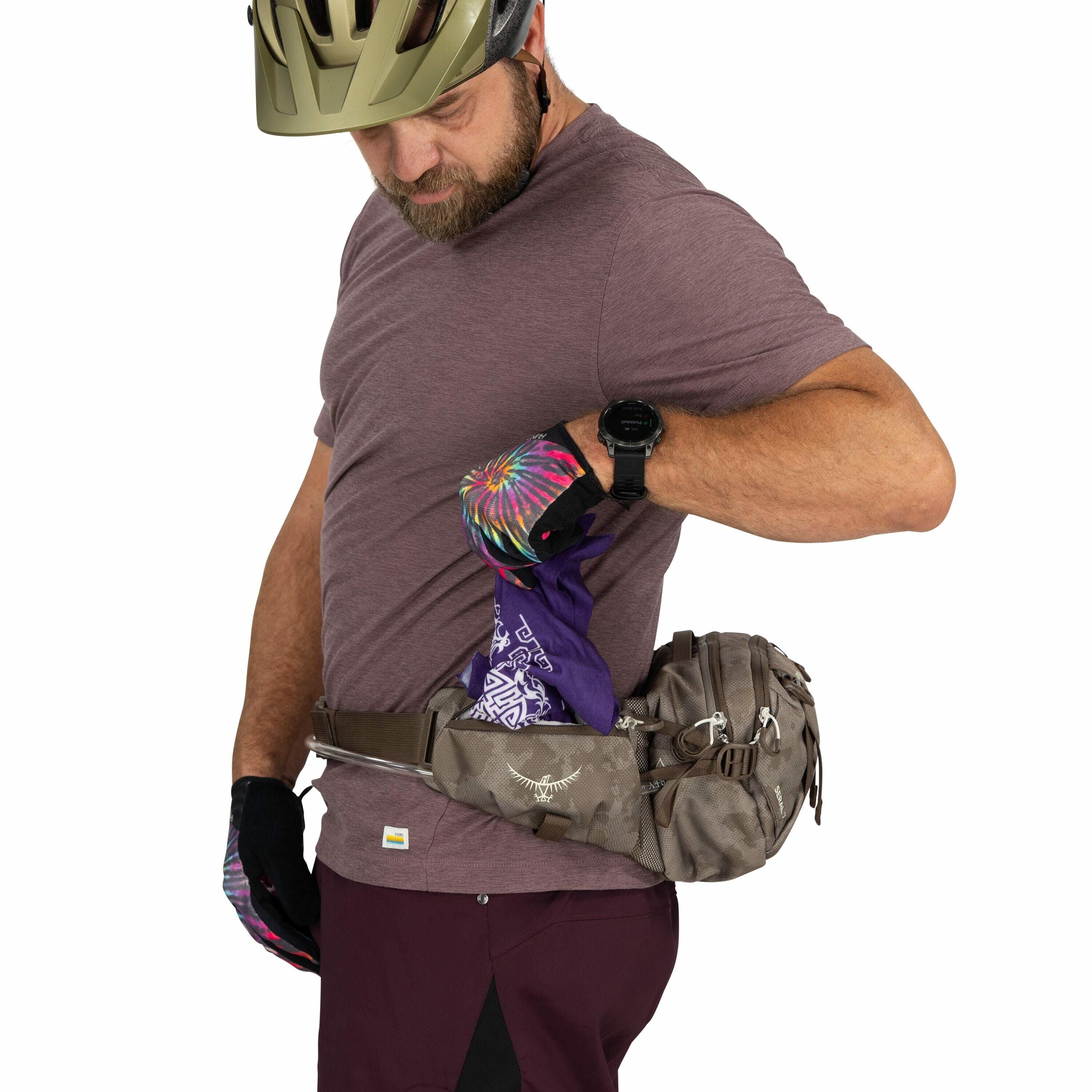 The image depicts a person wearing a gold bicycle helmet and a casual short-sleeve maroon t-shirt, with their attention focused on adjusting or retrieving an item from their waist pouch. The waist pack is a brown Osprey bag, secured around the person's wa