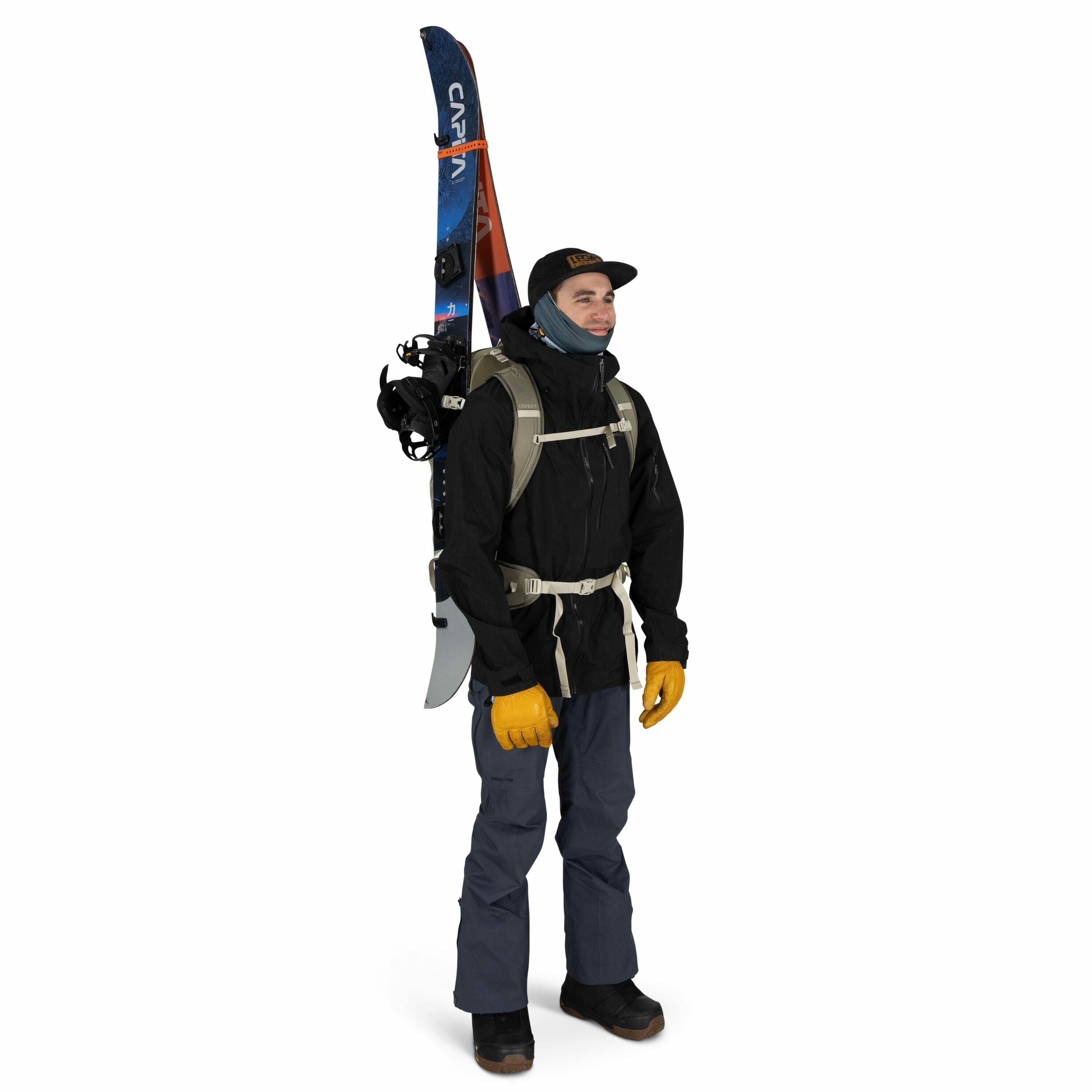 The image features a person dressed for outdoor adventure or possibly winter sports. They are wearing a black jacket, dark blue pants, and sturdy black boots. A pair of skis is strapped vertically to a light-colored backpack, suggesting preparedness for s