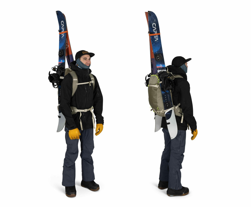 The image shows a person dressed in winter gear, prepared for a skiing or snowboarding adventure. The person is wearing a black jacket and blue pants, along with orange gloves and black boots. They have a grey backpack with ski equipment attached to it, i