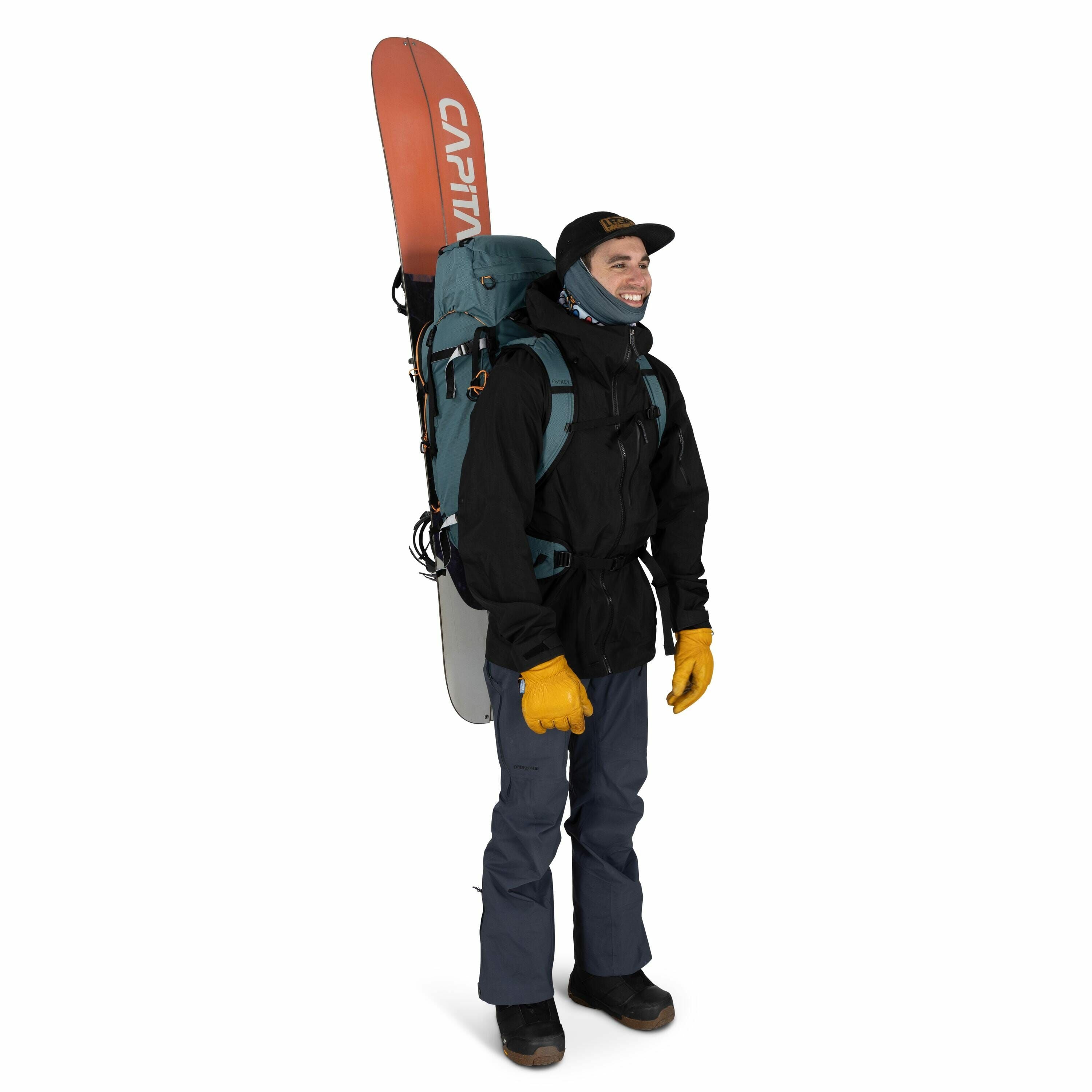 The image shows a person dressed in outdoor gear, likely prepared for a snowboarding or mountain adventure. They are wearing a black jacket, blue pants, and sturdy black boots, complemented by bright yellow gloves for protection against the cold. A blue b