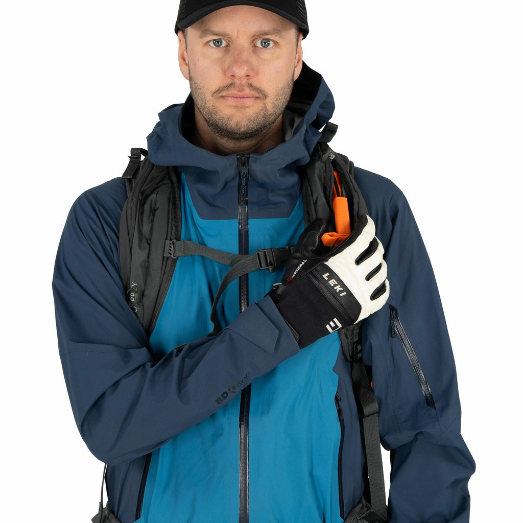 The image depicts a person wearing outdoor gear suitable for hiking or trekking. They are dressed in a dark blue waterproof jacket with a hood and layered underneath is a bright blue inner garment. The person is also wearing a black backpack that appears