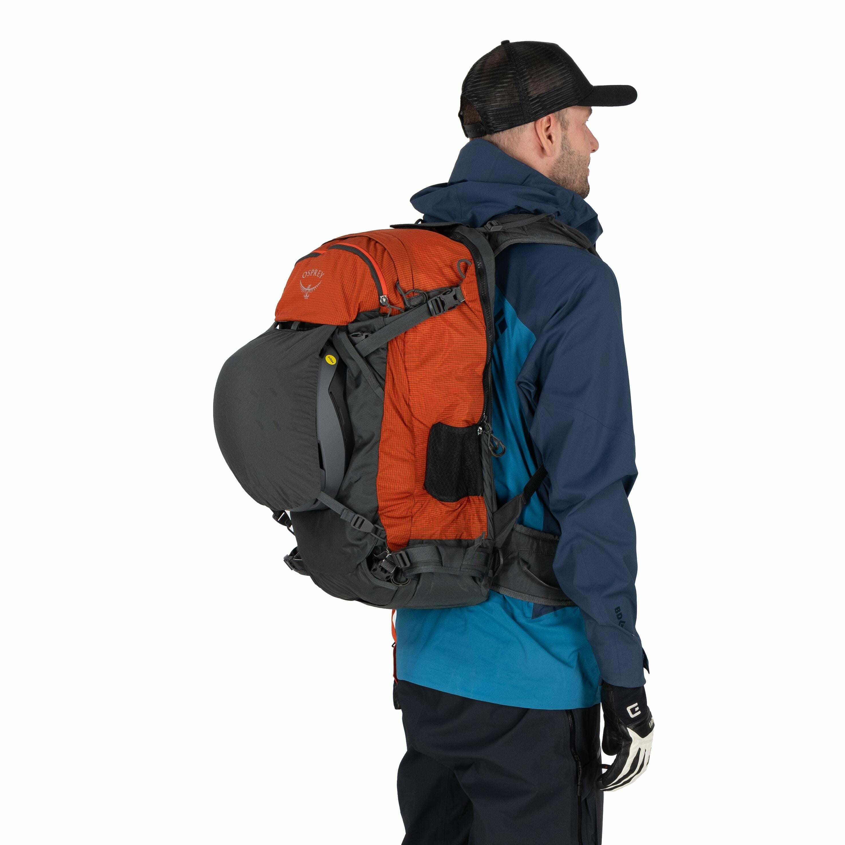 The image features an individual dressed in outdoor gear, likely preparing for a hiking or trekking adventure. They are wearing a dark blue jacket with a lighter blue shirt underneath and black pants. The person is carrying a large, multi-functional backp