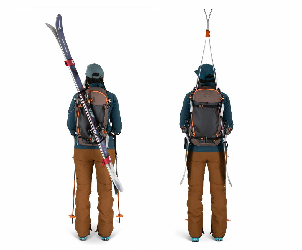 The image shows a person dressed in outdoor winter gear, viewed from the back. The person is wearing brown snow pants, a teal jacket, and a matching teal hat or cap. They have a gray backpack with orange accents, which is being used to carry a pair of ski