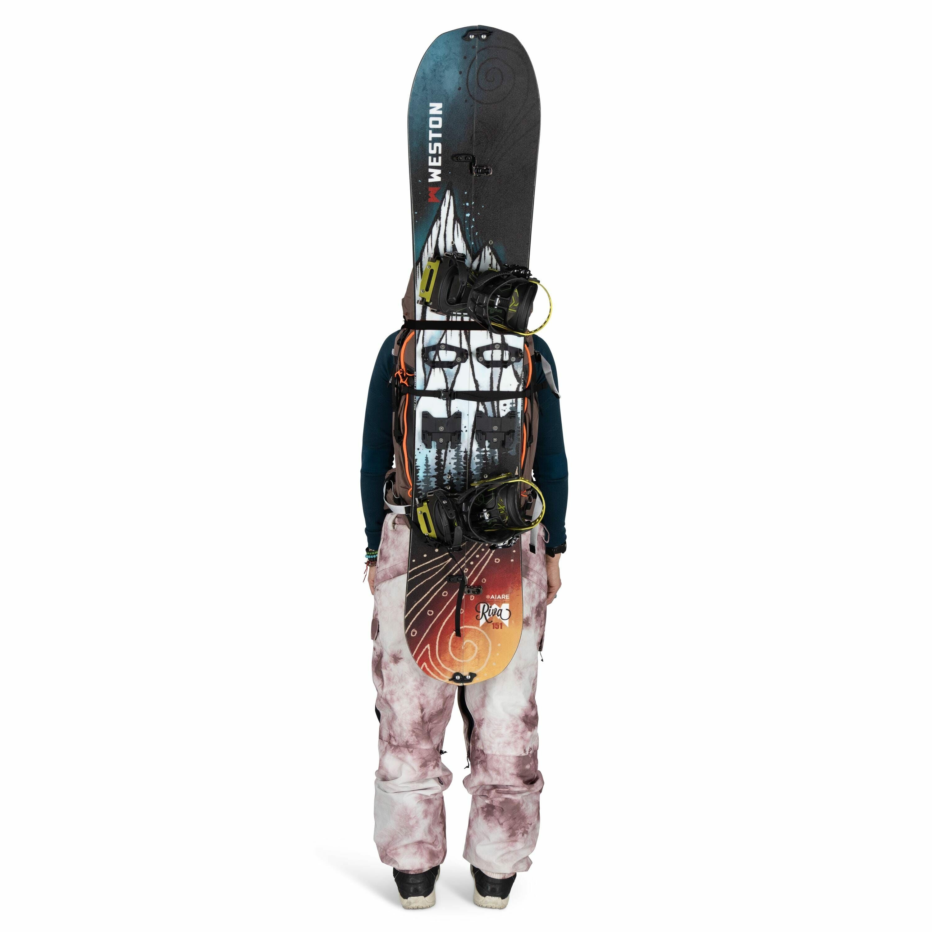 The image shows a person from behind, dressed in a winter outfit, standing upright. The person is wearing pink and white tie-dye snow pants and a dark blue long-sleeve top, both suitable for cold weather activities like snowboarding. They have a snowboard