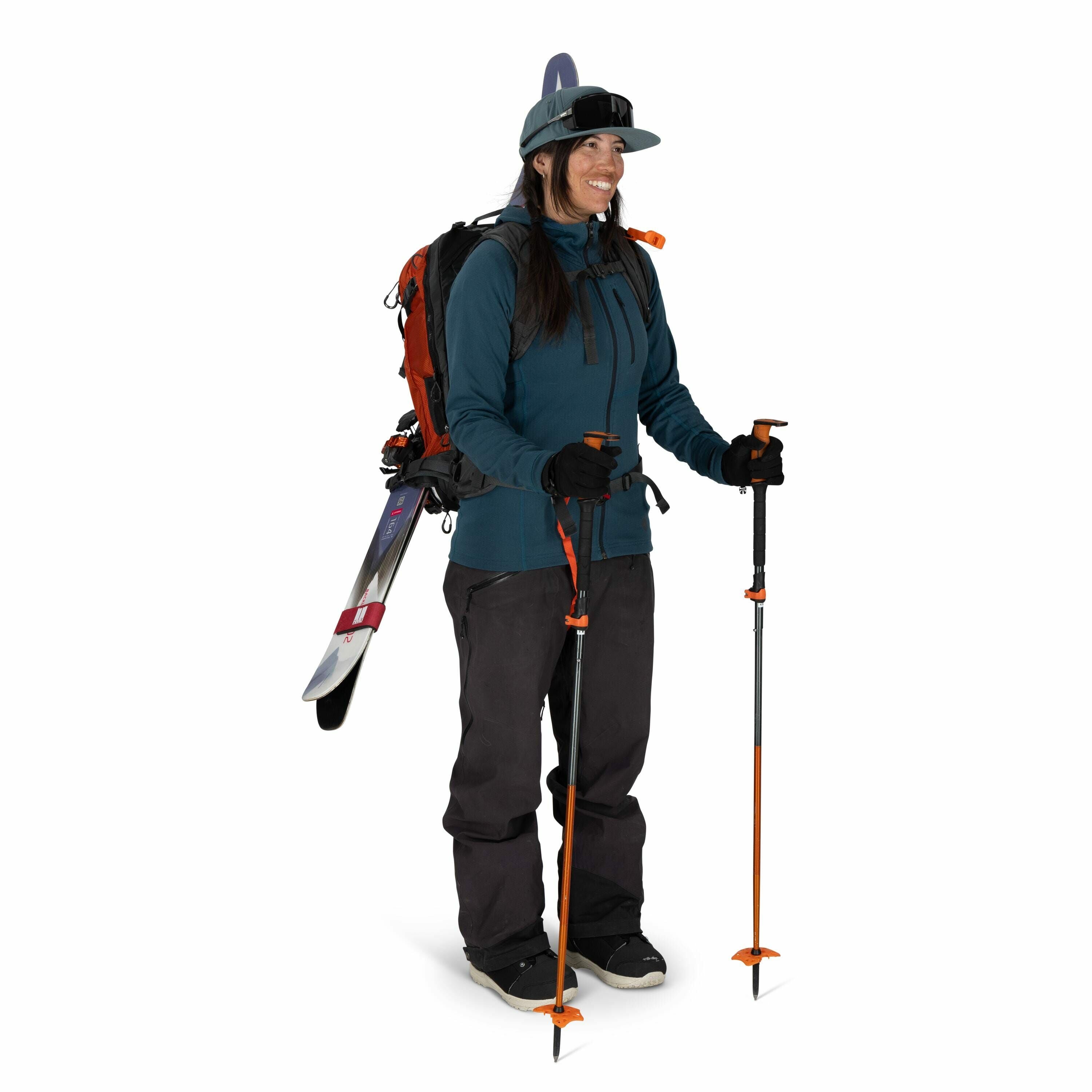 The image shows a person equipped for skiing or snowboarding in a winter setting. They are dressed in a teal jacket, dark pants, and black gloves, which provide warmth and protection against cold weather conditions. The person is holding two orange ski po